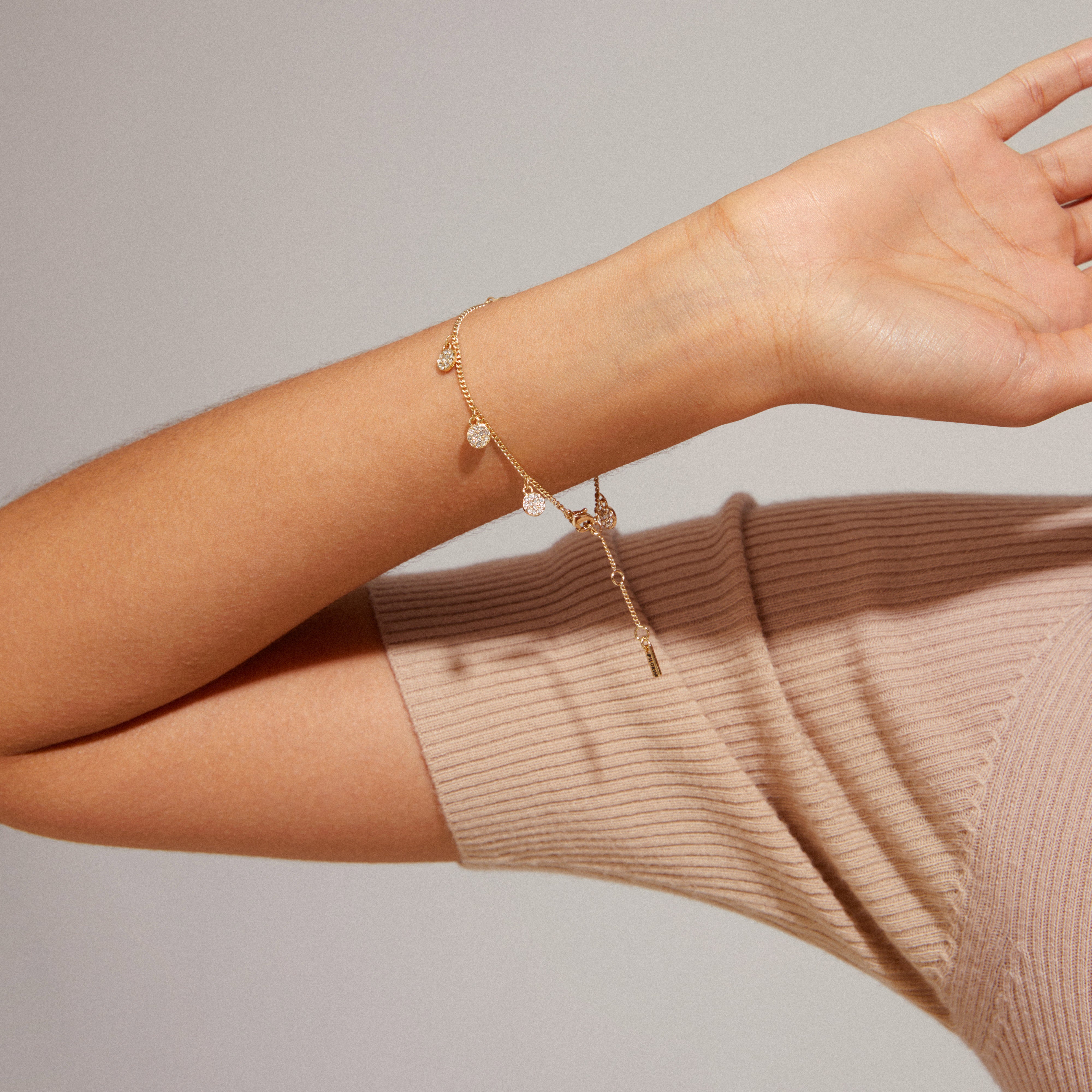 CHAYENNE crystal bracelet gold-plated with sparkling Preciosa crystals and small coin pendants, worn by a person in a tan sweater.
