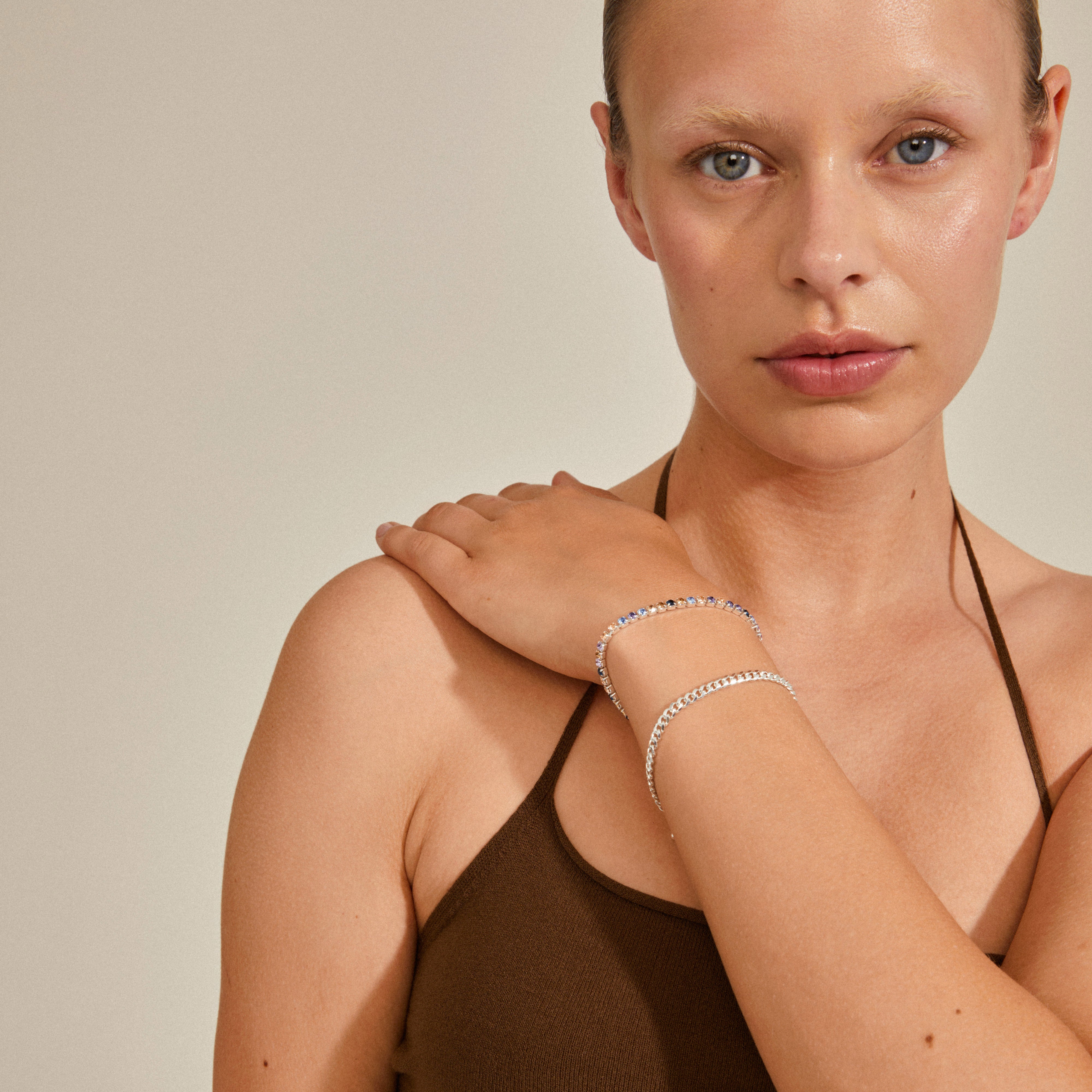 Woman wearing the REIGN bracelet, 2-in-1 set, silver-plated, featuring a classic curb chain paired with blue and champagne Preciosa crystals, capturing a stylish urban look.