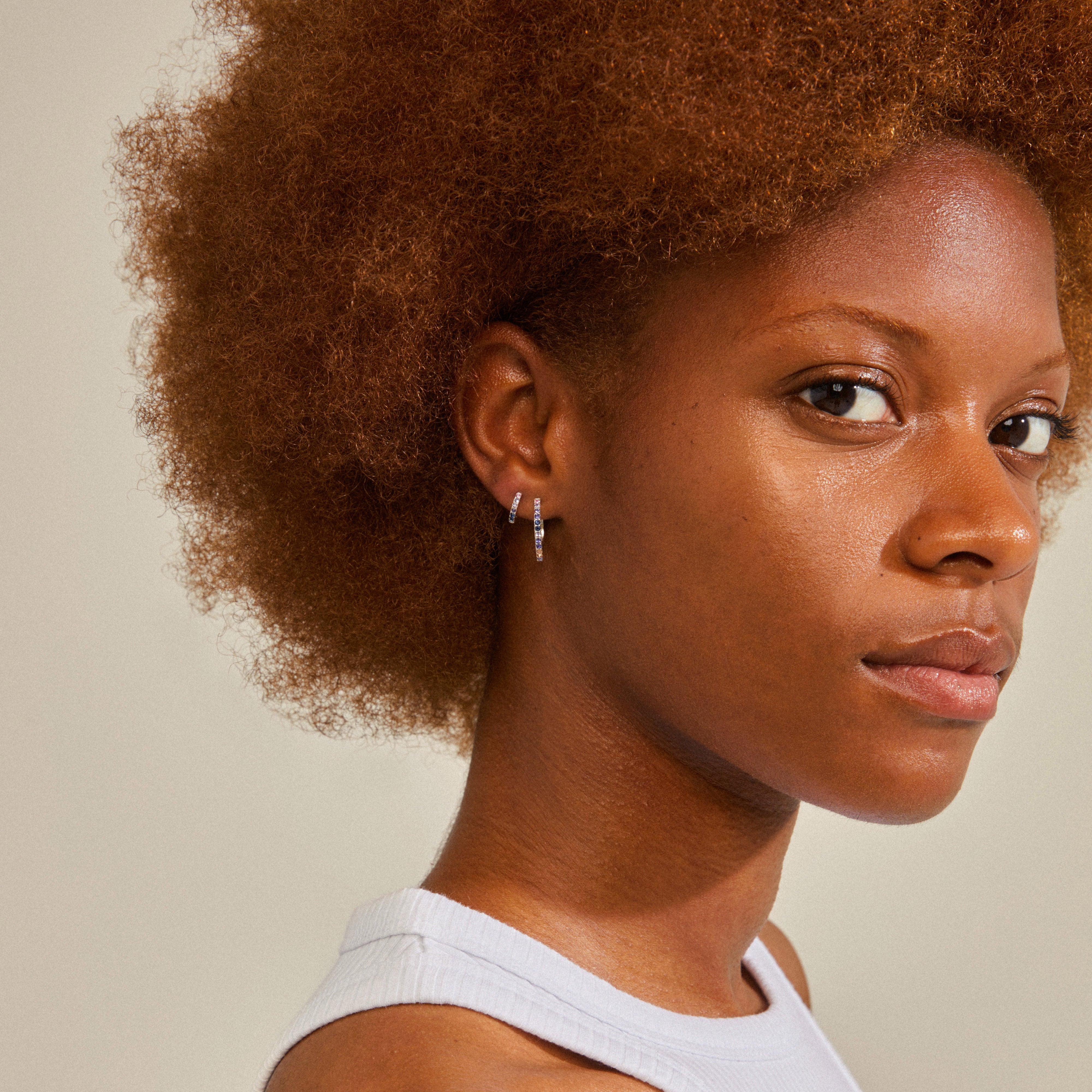 Silver-plated REIGN hoops, adorned with blue and champagne Preciosa crystals, worn by a woman with curly hair. Perfect for both casual and glam occasions.