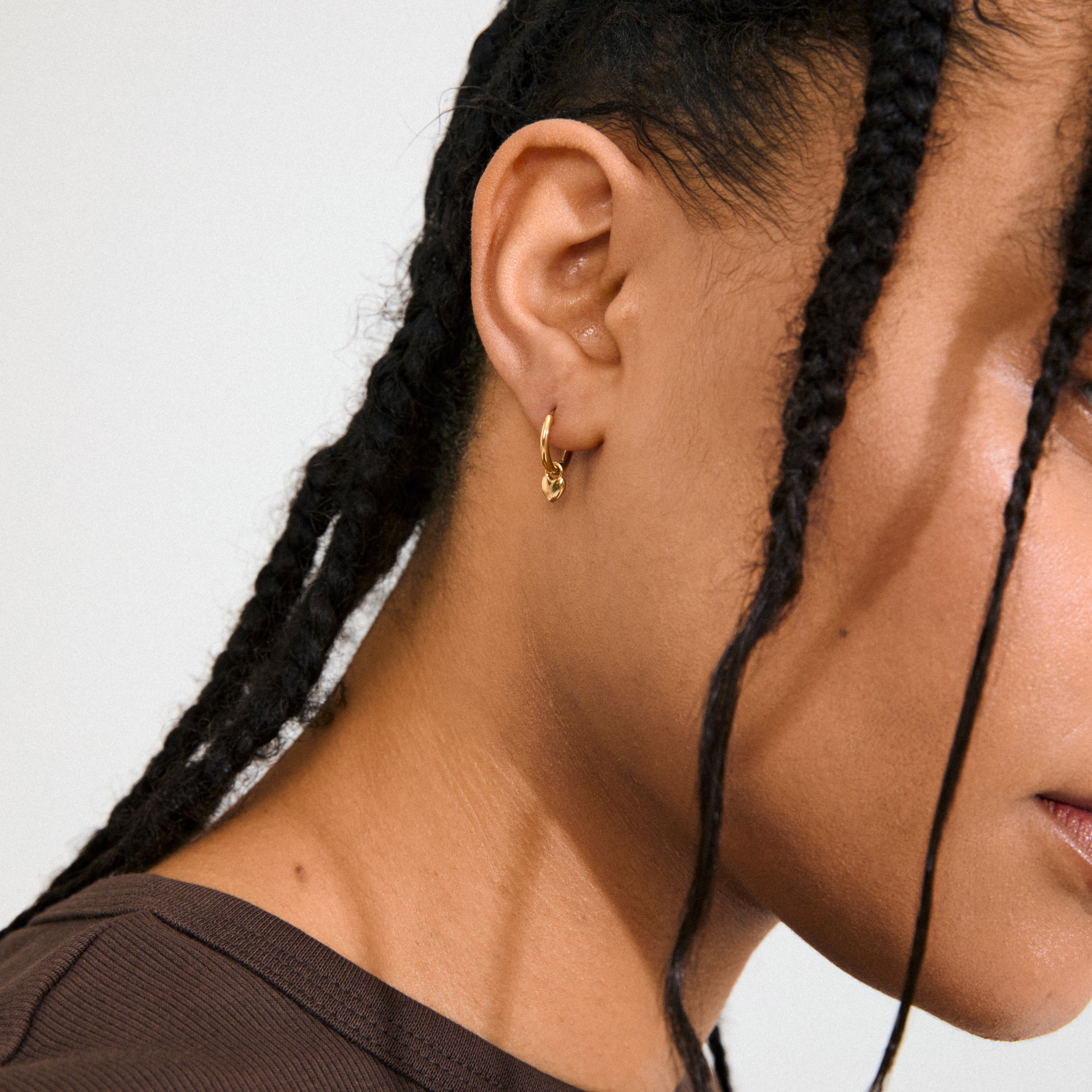 ALAIA gold-plated huggie hoops with detachable heart pendants, offering a versatile, romantic look. Perfect for everyday wear and special occasions. Made from 99% recycled material.
