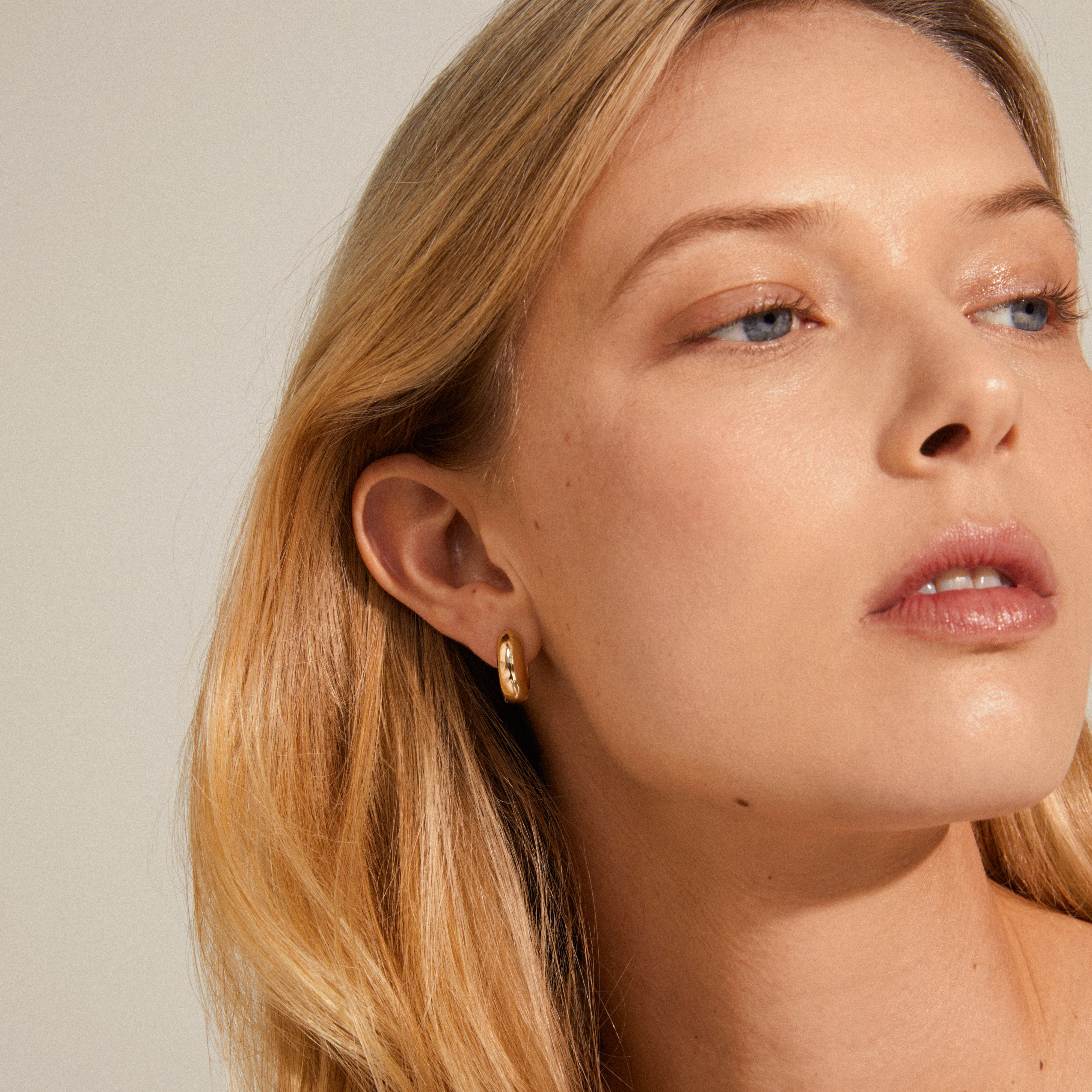 Close-up of a woman wearing Pilgrim's MINE chunky gold-plated huggie hoops, showcasing their shiny, elegant design.