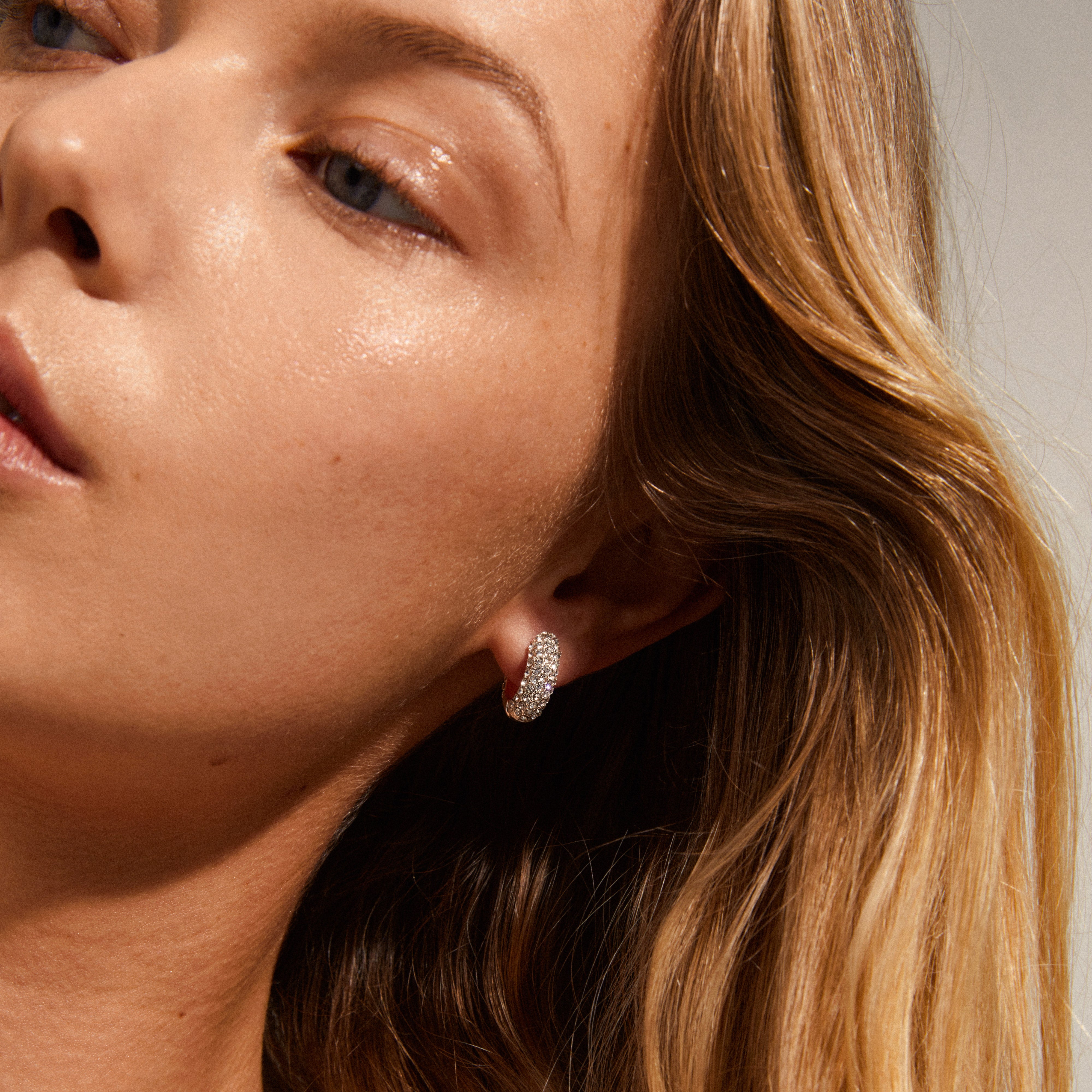 LONA chunky crystal huggie hoops, silver-plated, elegantly adorn a woman's ear, showcasing sparkling Preciosa crystals for an exclusive, classy look.