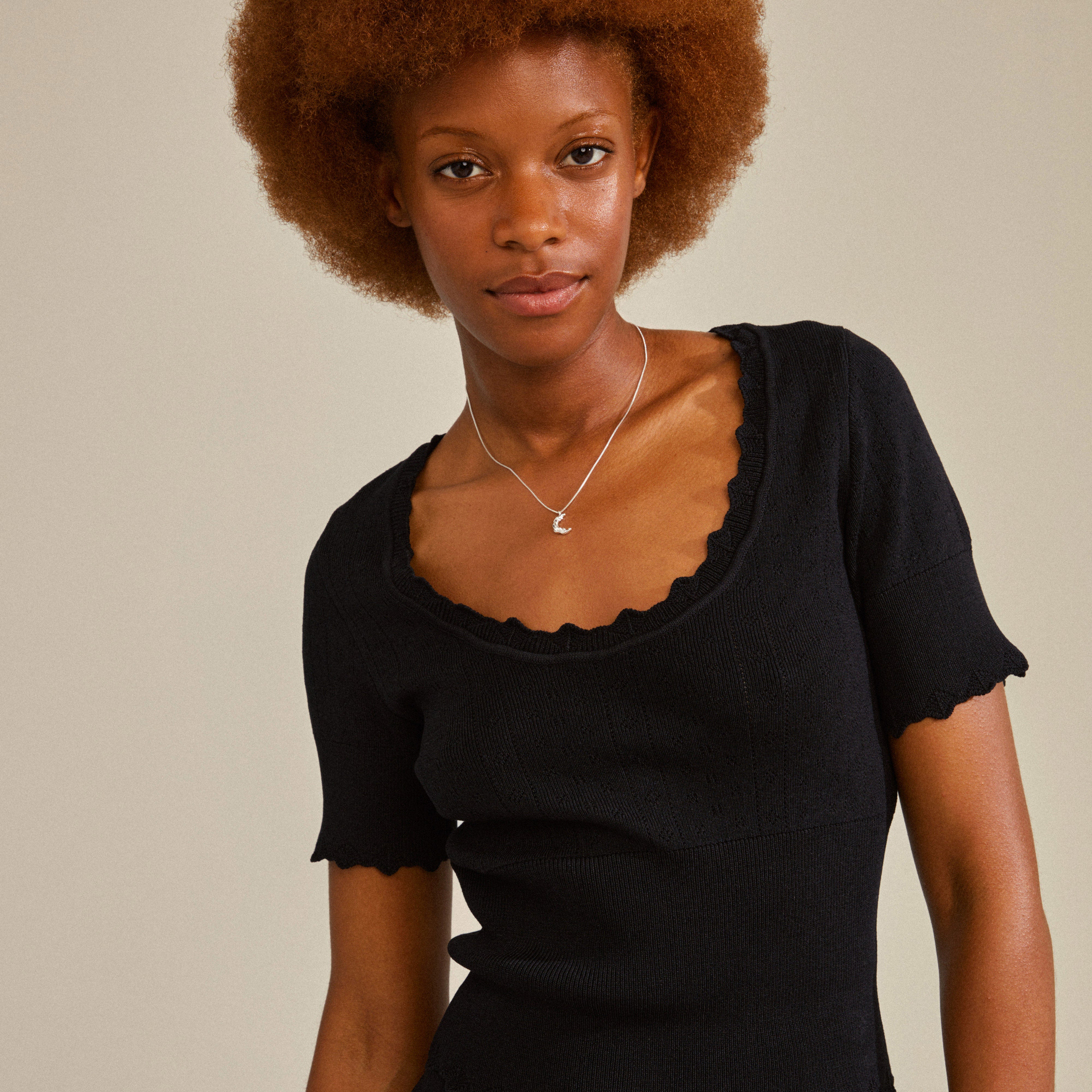 Young Black woman wearing a REMY necklace silver-plated, featuring a delicate crescent-moon pendant on a silver chain, styled with a black knit top.