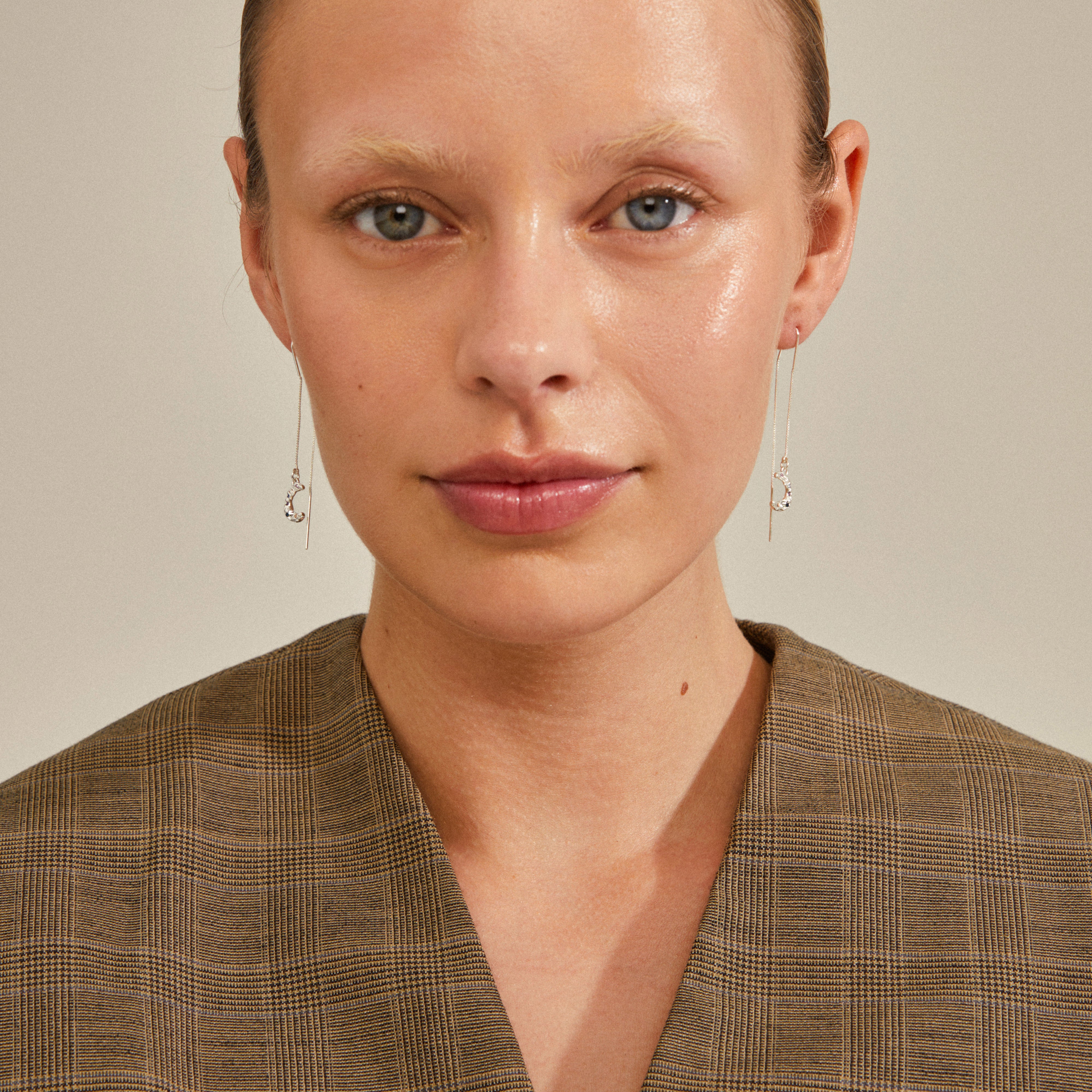 Close-up of a woman wearing REMY silver-plated chain earrings with a half moon pendant, highlighting their delicate, uneven design and minimalist appeal.