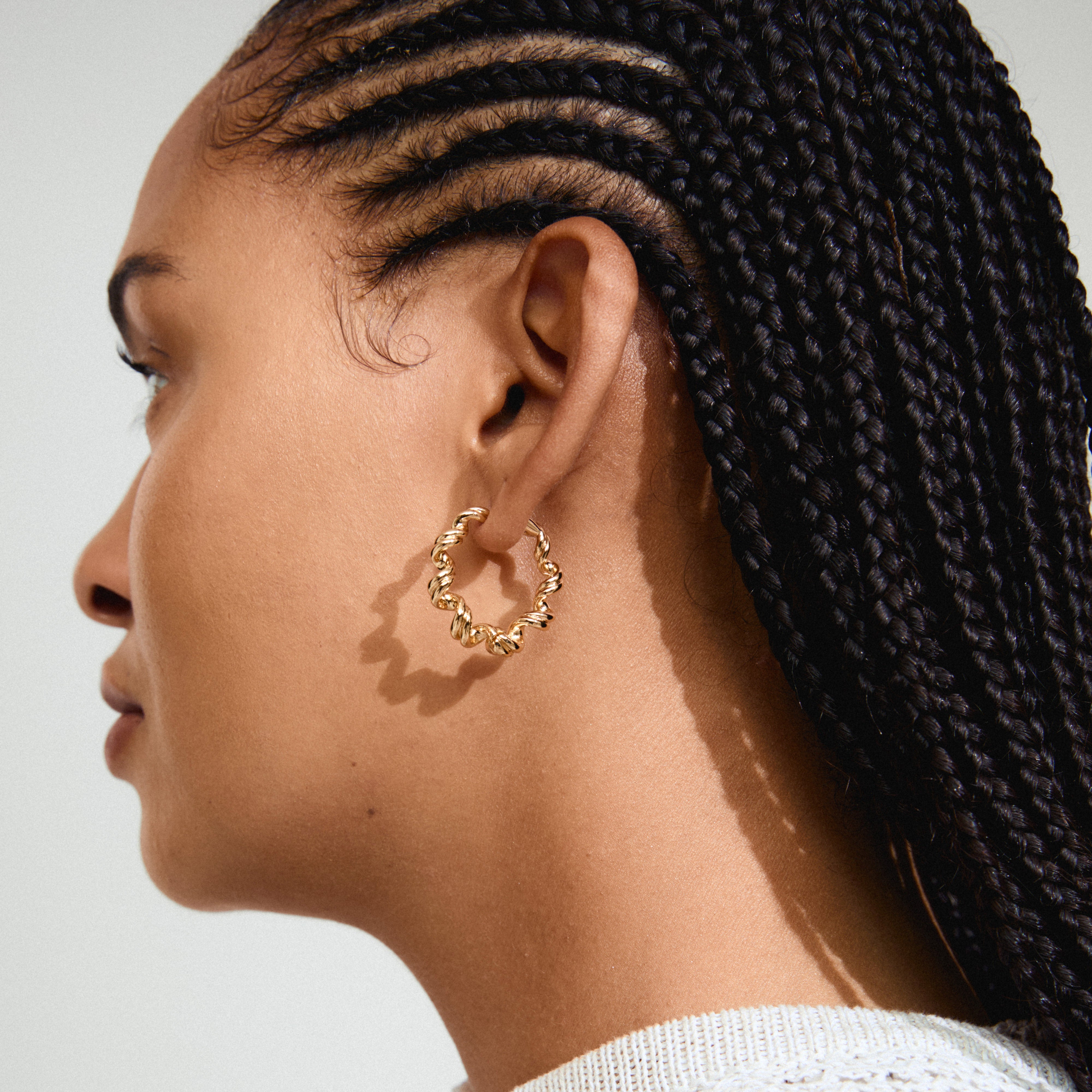 LARISA earrings gold-plated, featuring twisted spiral design, adorn a woman's ear with braided hair, capturing Pilgrim's trendy, handcrafted aesthetic.