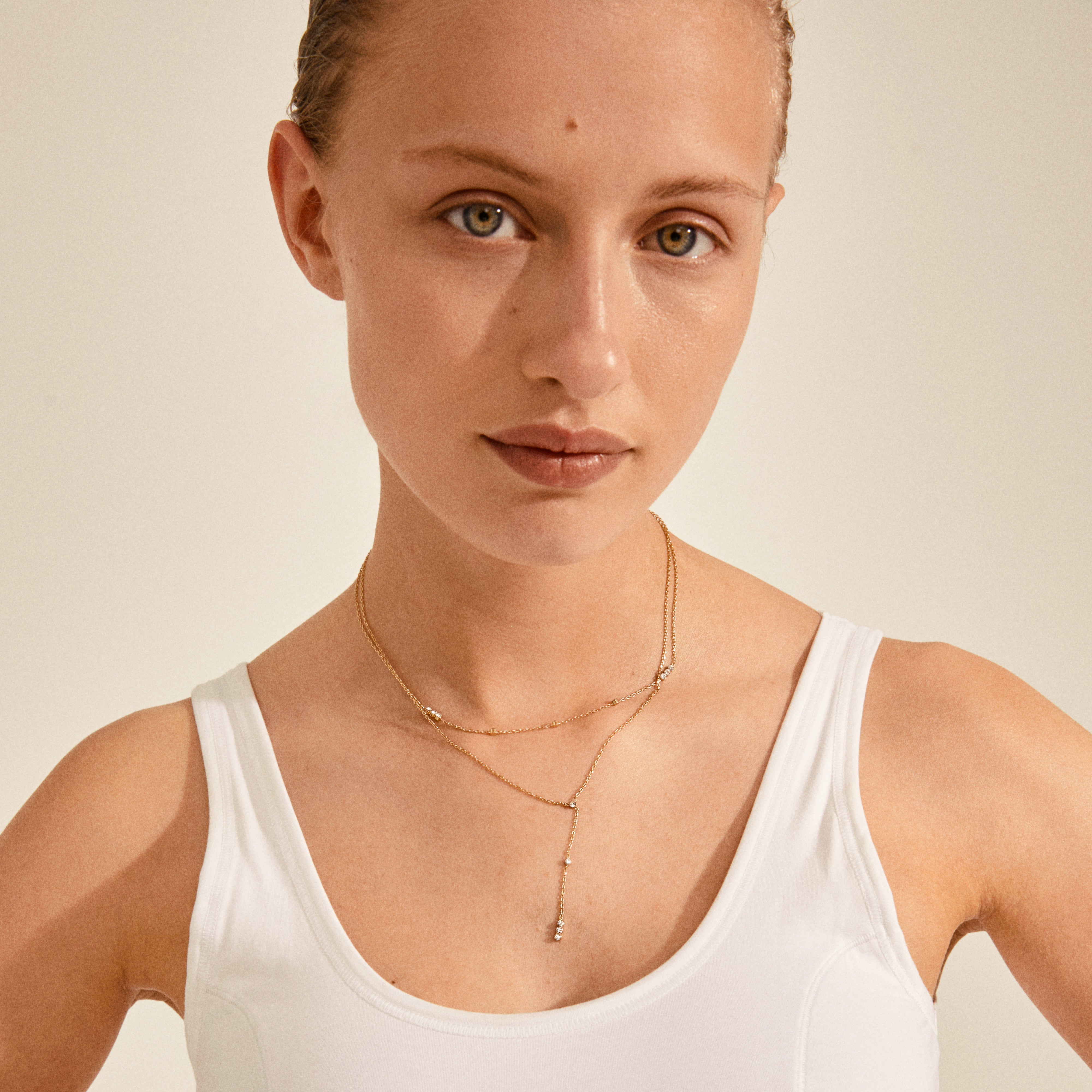 KAMARI crystal chain necklace gold-plated adorns a woman in a white tank top, showcasing its slender chain and sparkling crystals as a perfect party accessory.