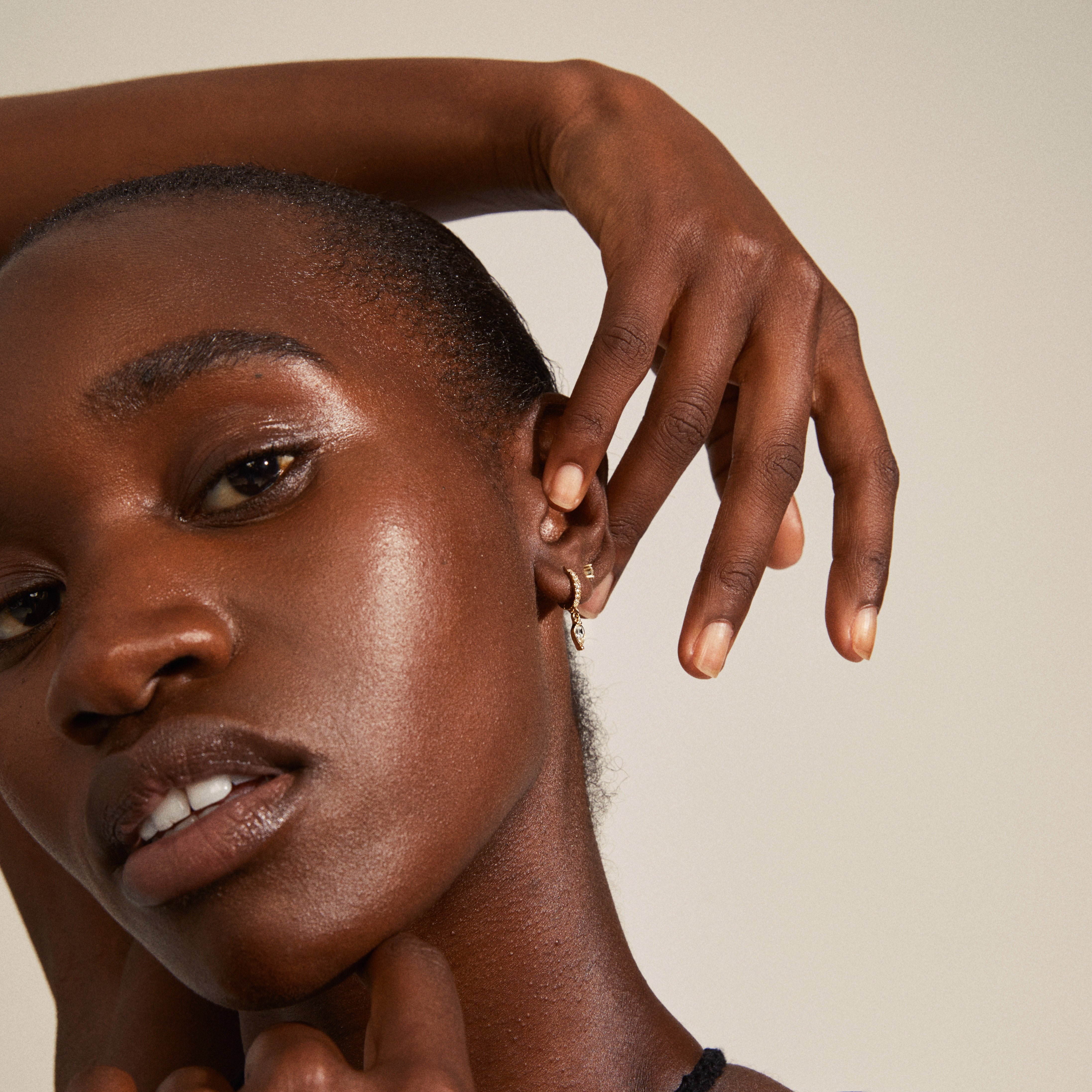 ELZA crystal earrings 2-in-1 set gold-plated, featuring small ear studs and huggie hoops with teardrop pendants, worn by a woman with her hand near her face.