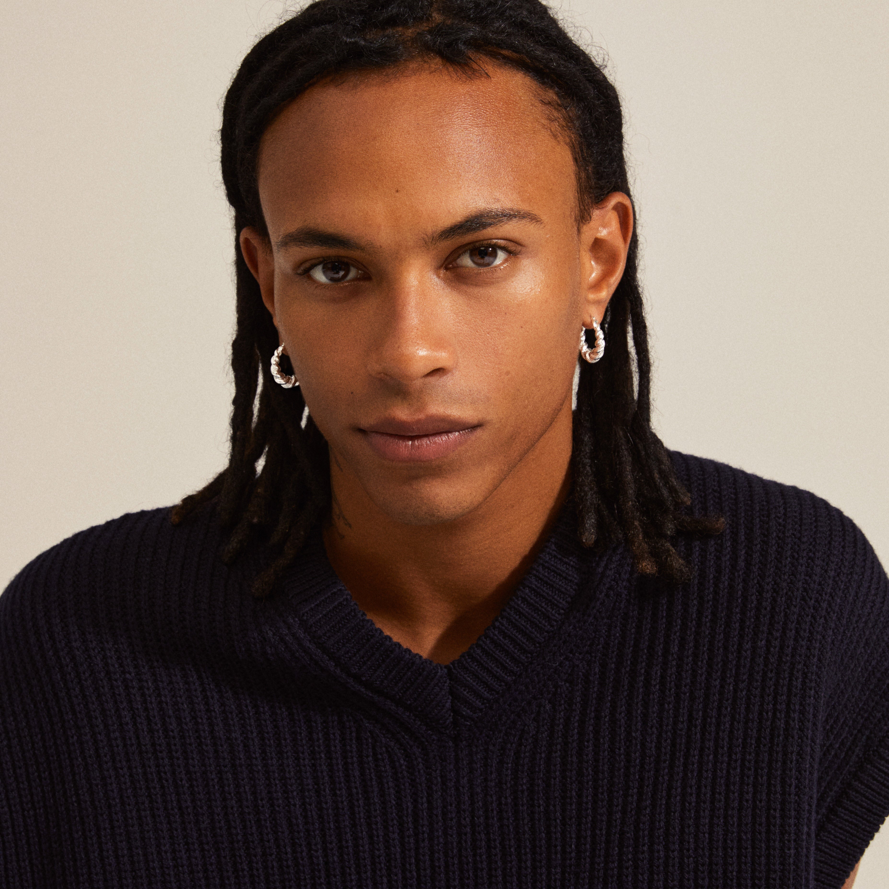 Man with dreadlocks wearing EILEEN twirl hoop earrings, showcasing the silver-plated, twisted design inspired by waves, embodying a boho and adventurous style.