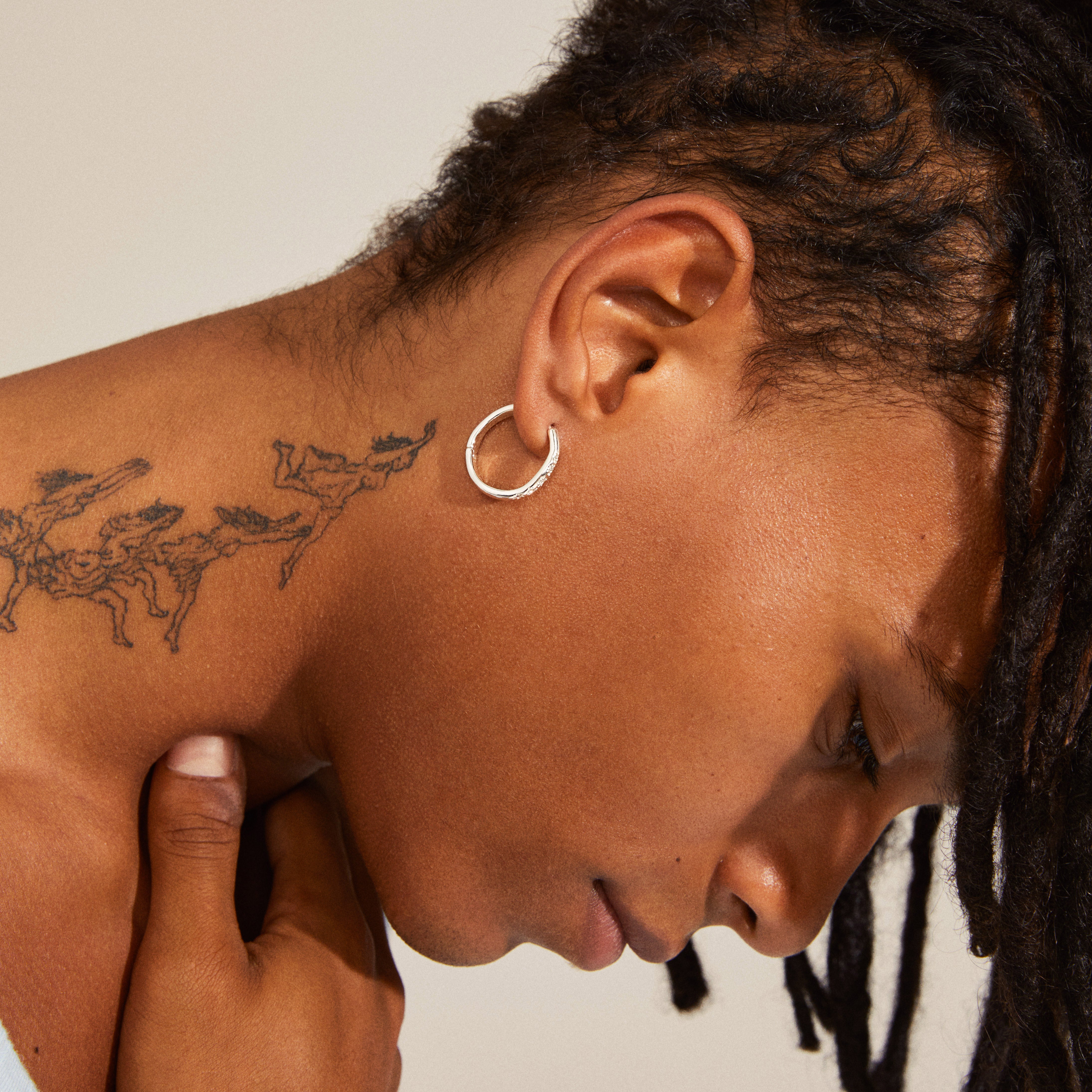 Close-up of person wearing silver-plated EDURNE crystal hoop earrings, showcasing their organic silhouette and engraved floral details with Preciosa crystals.