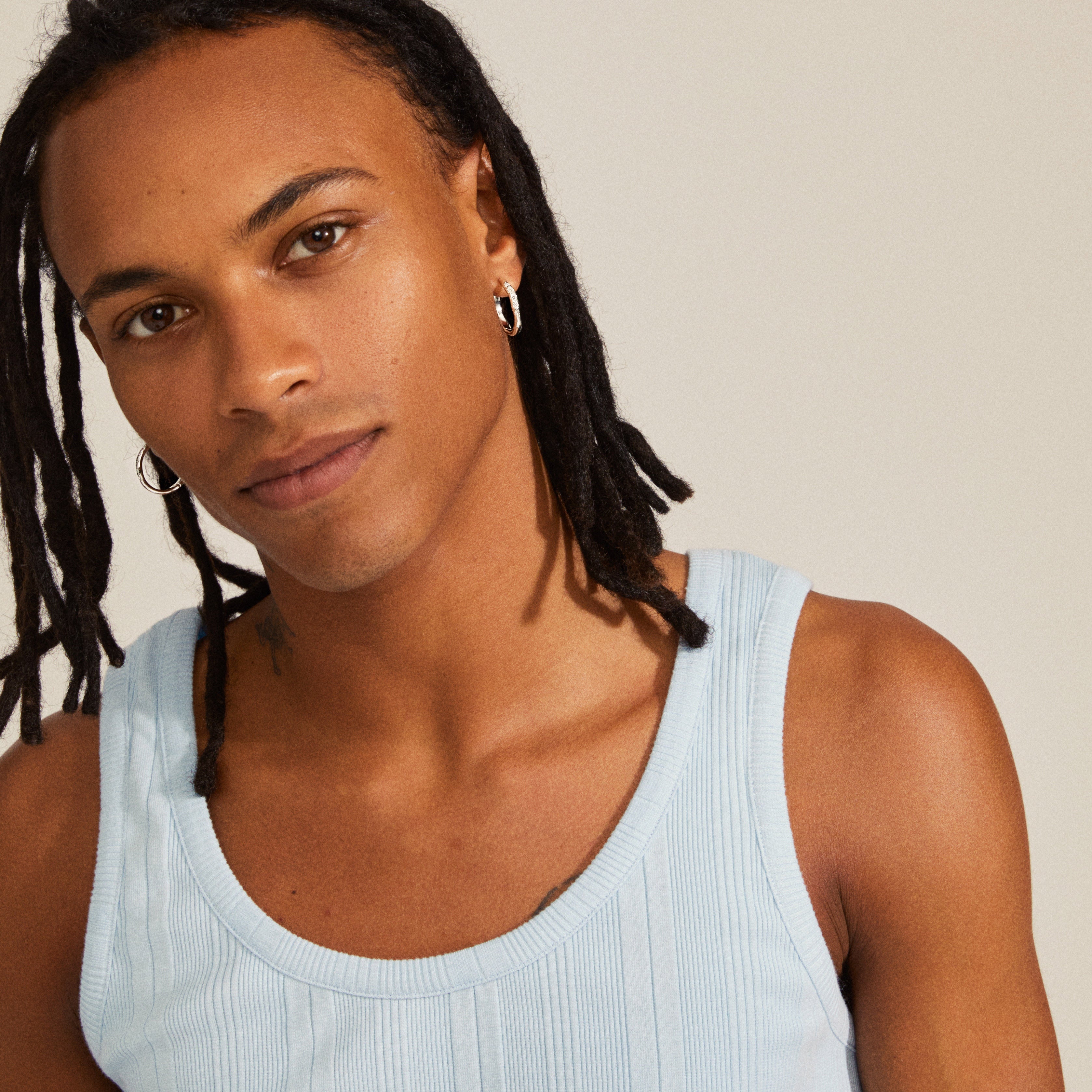 Man with dreadlocks wearing a white tank top displaying Edurne crystal hoop earrings, silver-plated with organic silhouette and floral engravings, embodying nature-inspired elegance.