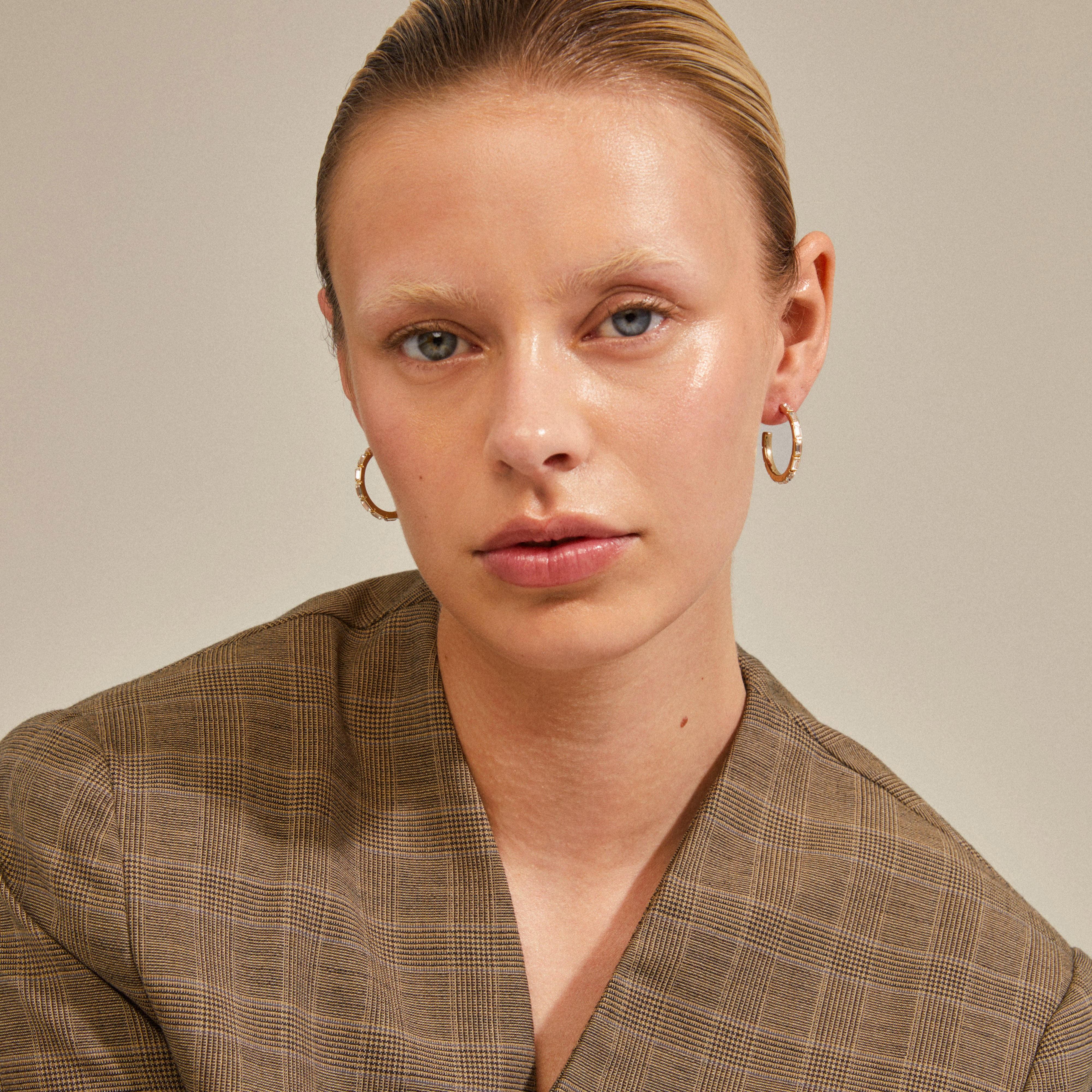 Close-up of a woman wearing RUE recycled gold-plated hoops, showcasing their sparkling glass stones and elegant design. Perfect for adding glam to any outfit.