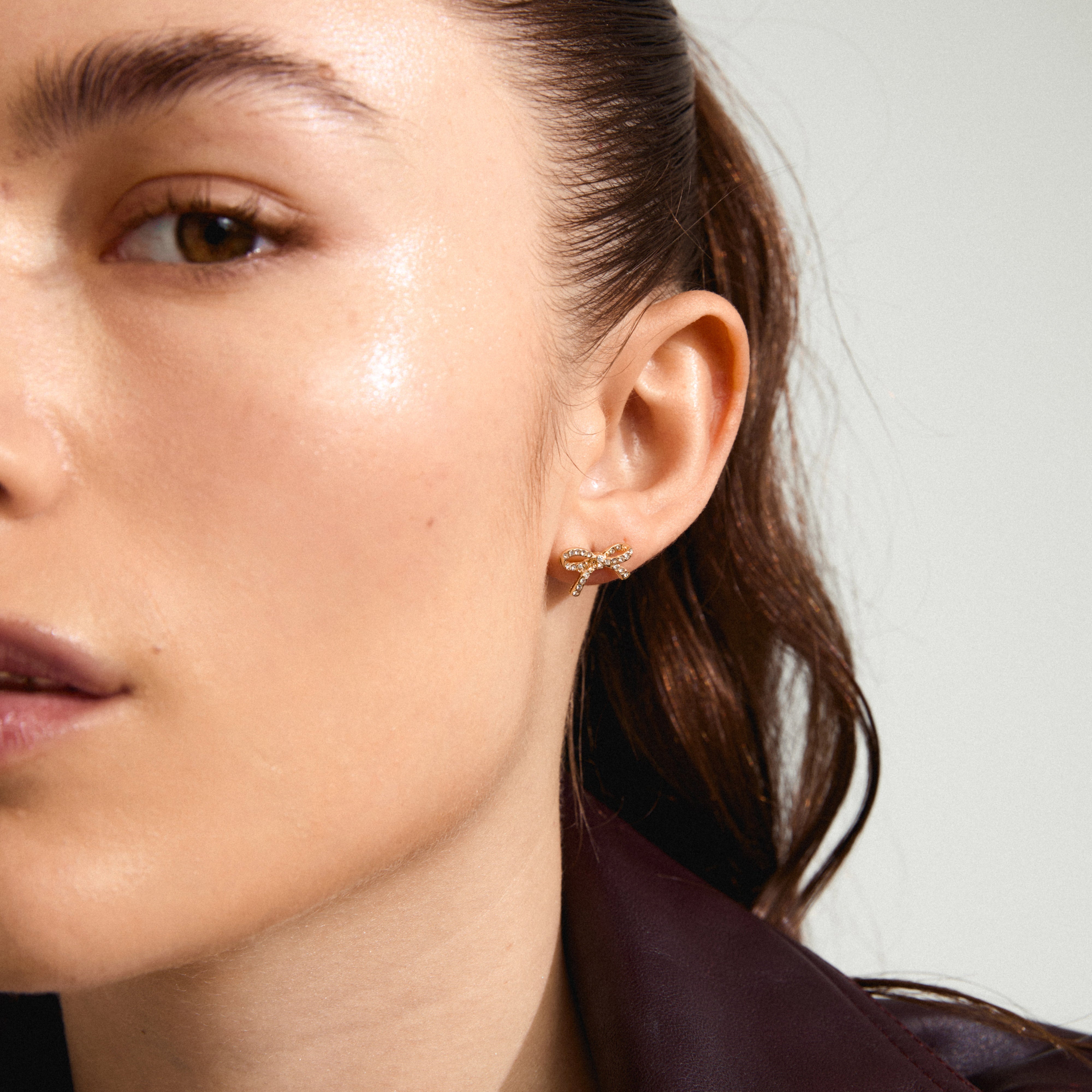 CATHARINA earrings gold-plated, bow-shaped with Preciosa crystals, adorn a woman's ear, showcasing trendy, recycled Danish jewelry from Pilgrim.