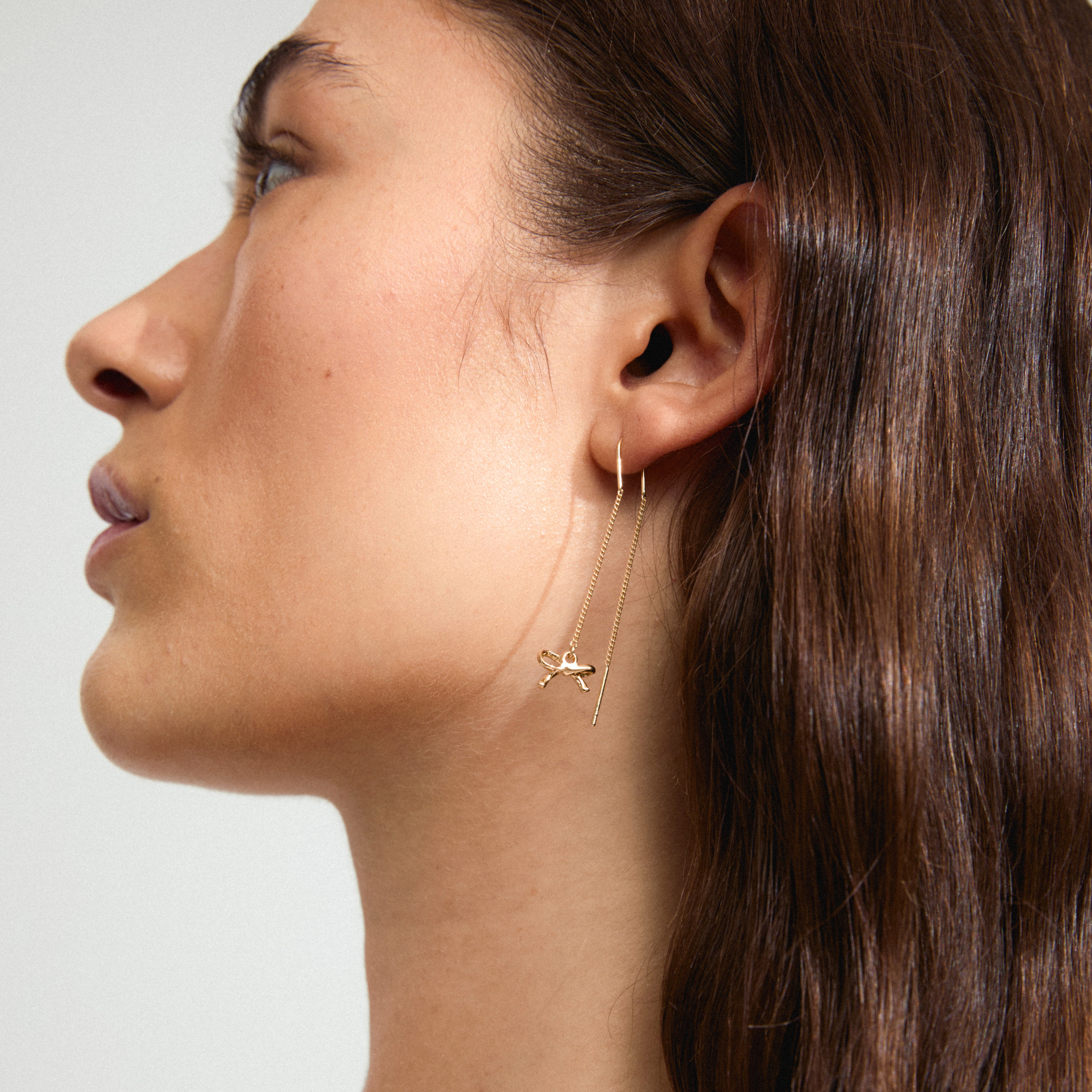 Side view of a woman wearing LYSANDRA gold-plated chain earrings with small bow pendants, showcasing their elegant, trendy design.