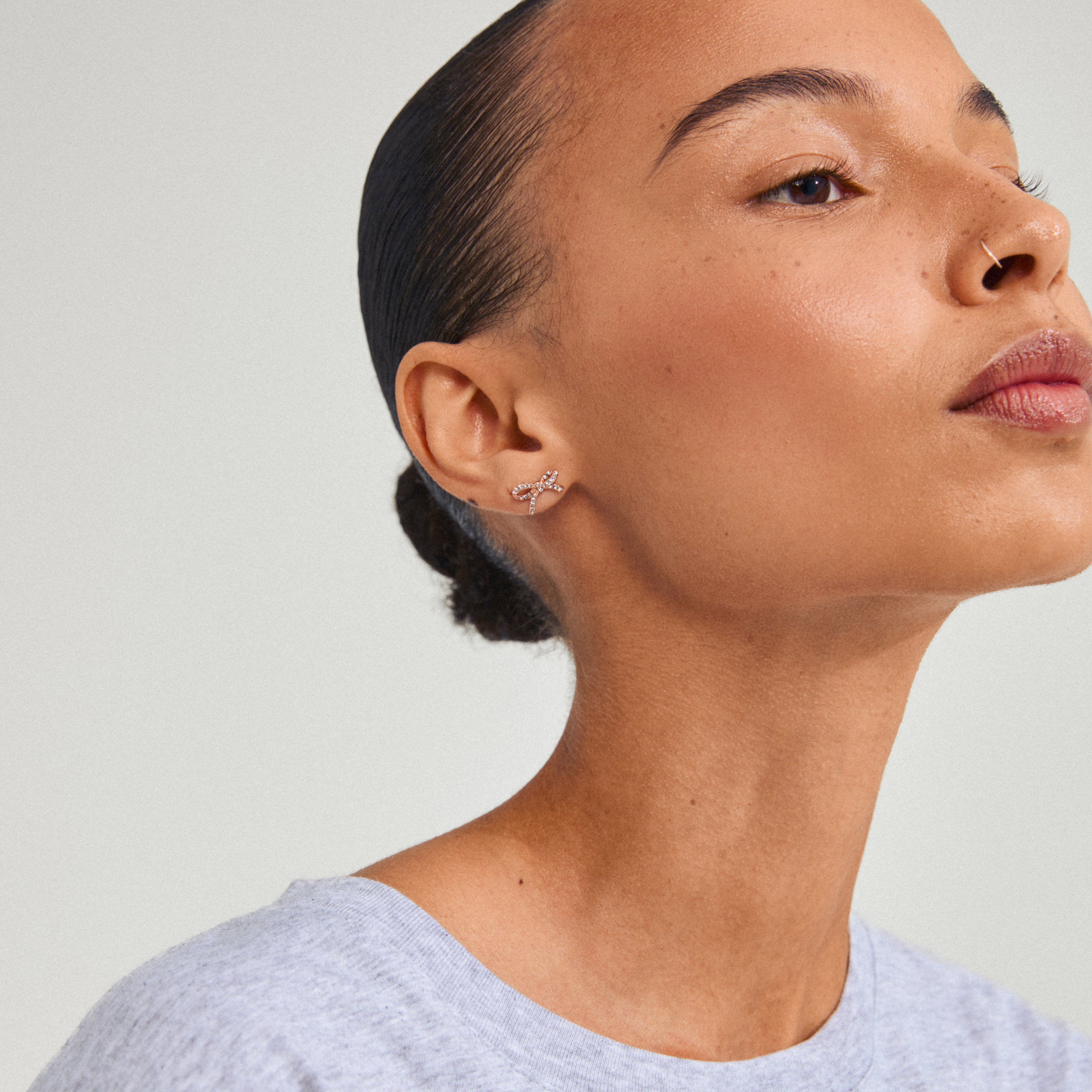 CATHARINA earrings, rose gold-plated micro studs with sparkling Preciosa crystals, showcased on a woman's ear. Trendy and sustainable, perfect for a subtle summer sparkle.
