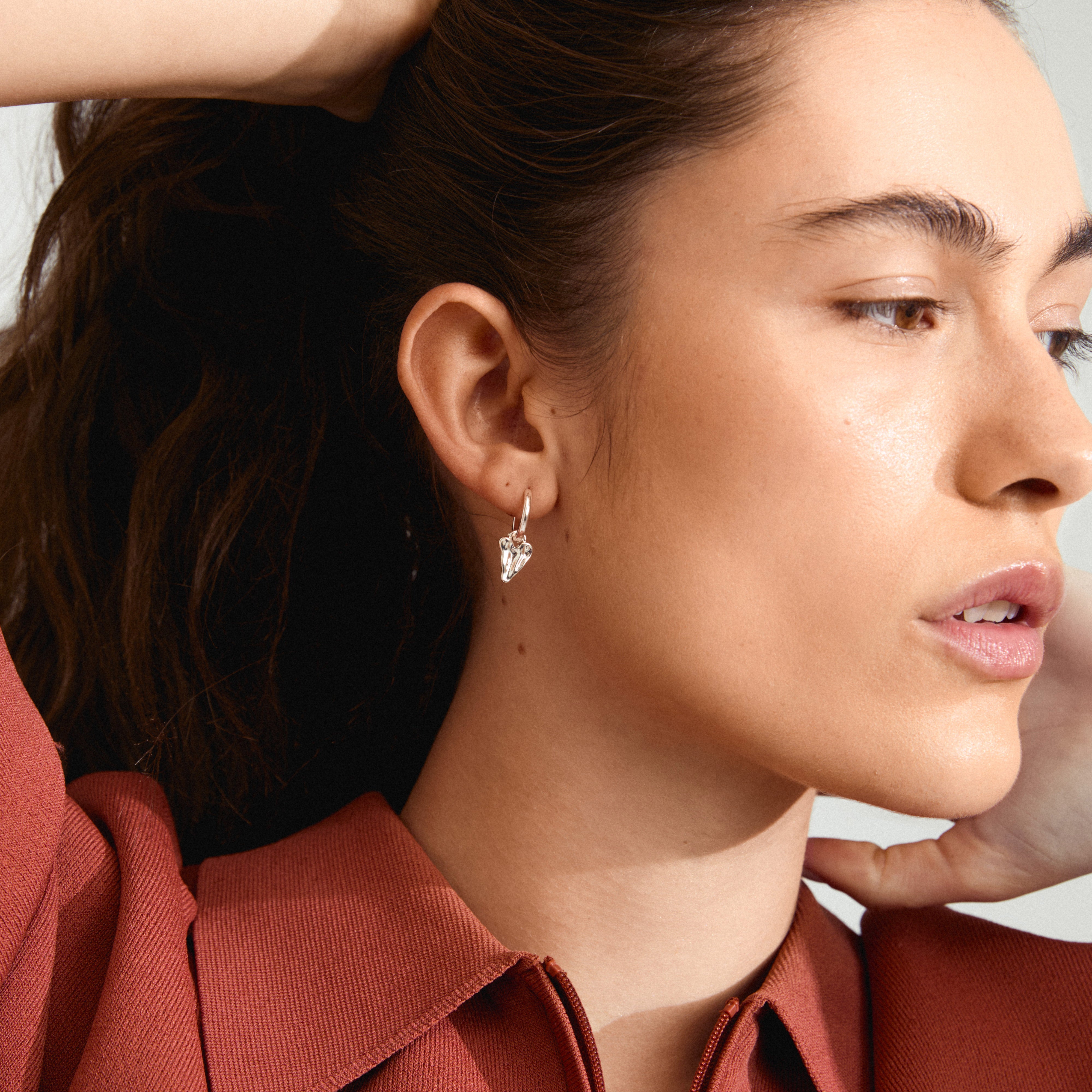JULES earrings silver-plated feature classic hoops with silver heart pendants, visible on a woman. Stylish, eco-friendly, perfect for mix-and-match looks.