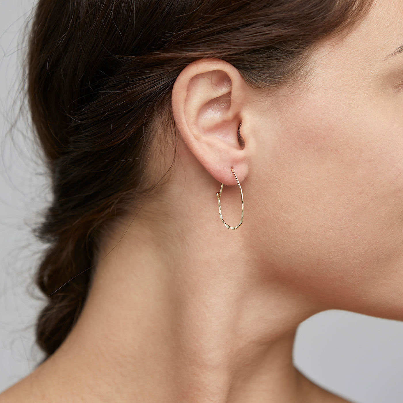 OLENA earrings gold-plated, showcasing a rustic hammered finish on a woman's ear, exuding a confident, trendy style.