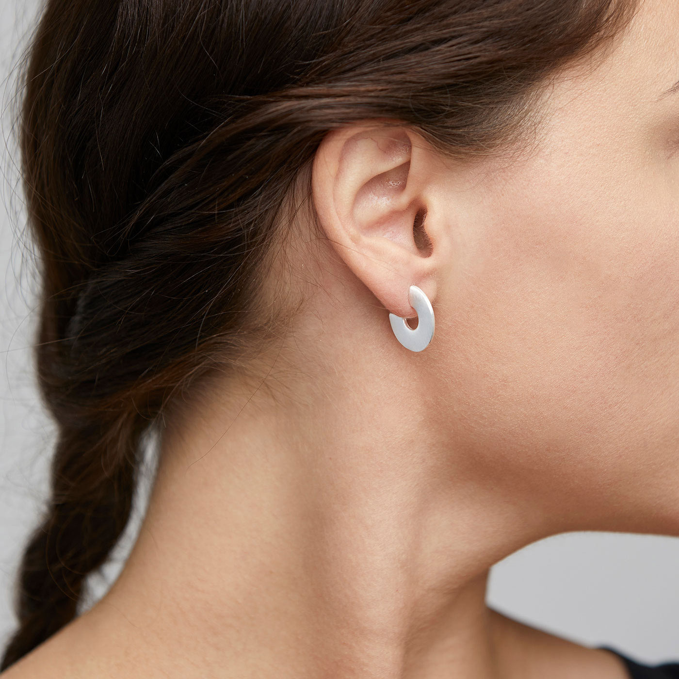 Close-up of VIVIAN silver-plated earrings with a broad, brushed matte finish on a woman's ear, showcasing their chic and distinctive style.