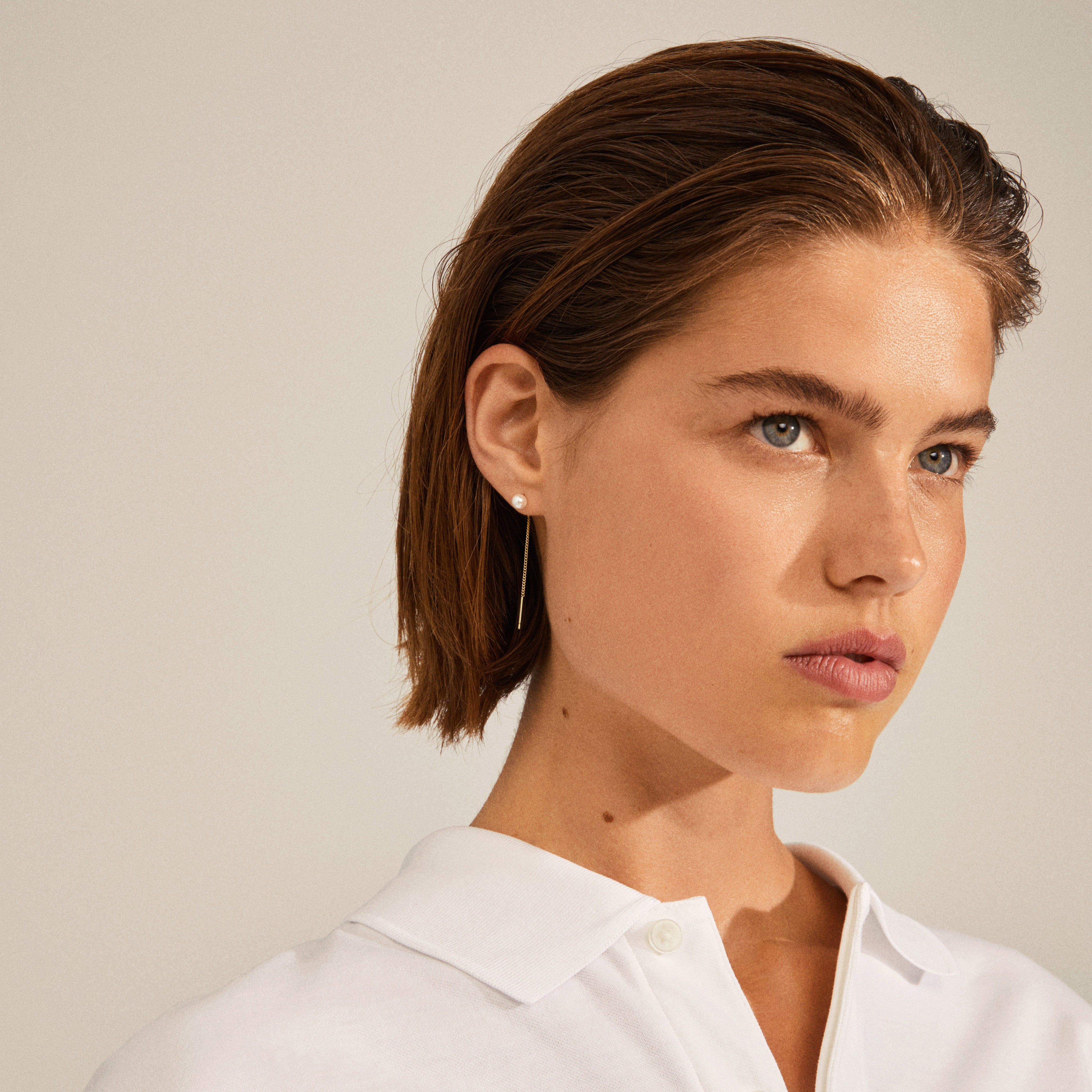 Woman wearing ELBA long chain pearl earrings, featuring a white pearl front and a gold-plated chain adding movement behind the ear.