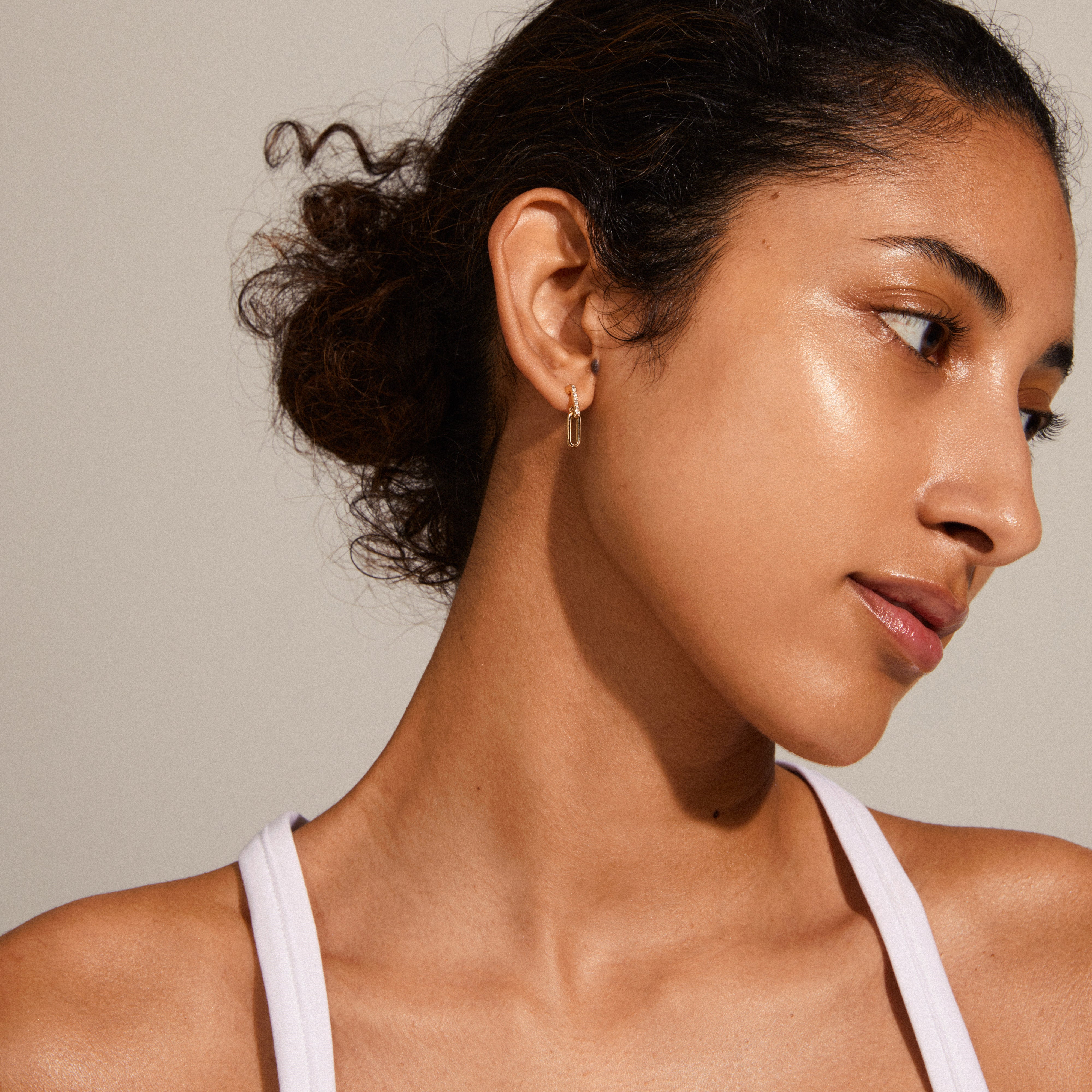 ELISE gold-plated oval link crystal earrings, featuring industrial shapes and shiny crystals, adorn a woman's ear, capturing elegance and modern style.