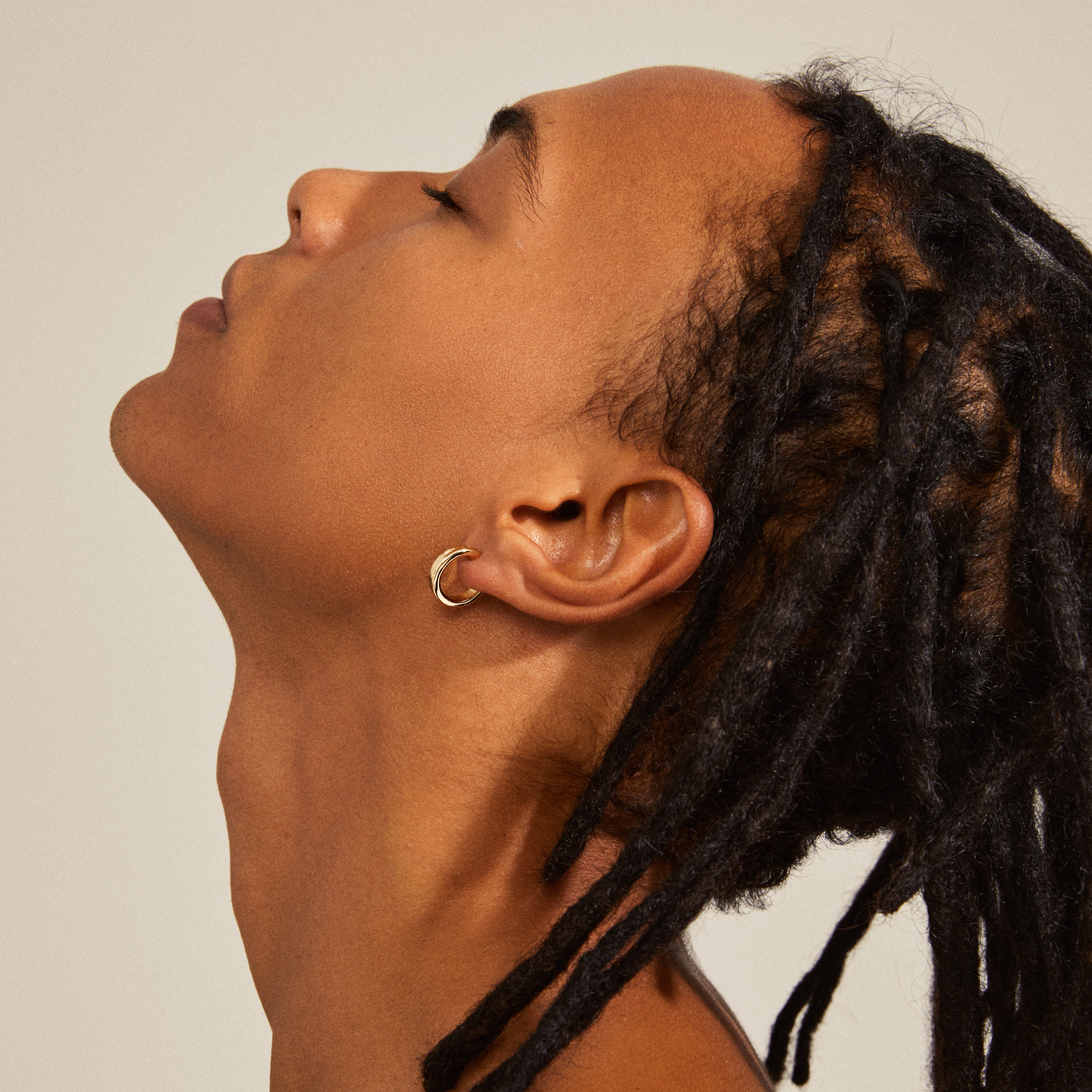 Efia gold-plated huggie hoop earrings, engraved with starry details, worn by a person with dreadlocks.