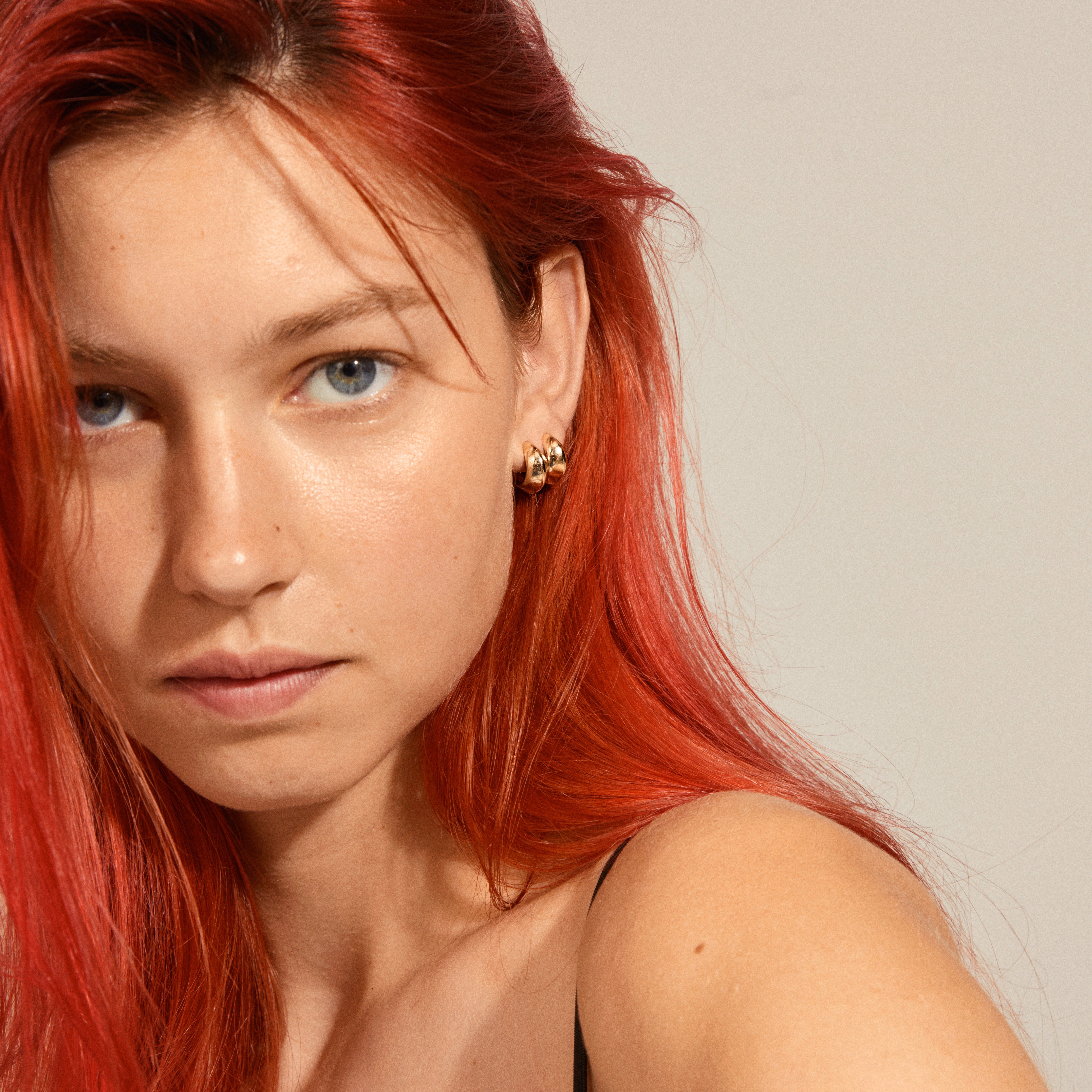 Close-up of a woman wearing Pilgrim's Edwina chunky huggie hoop earrings, gold-plated, showcasing their elegant, curved design and retro-inspired style.