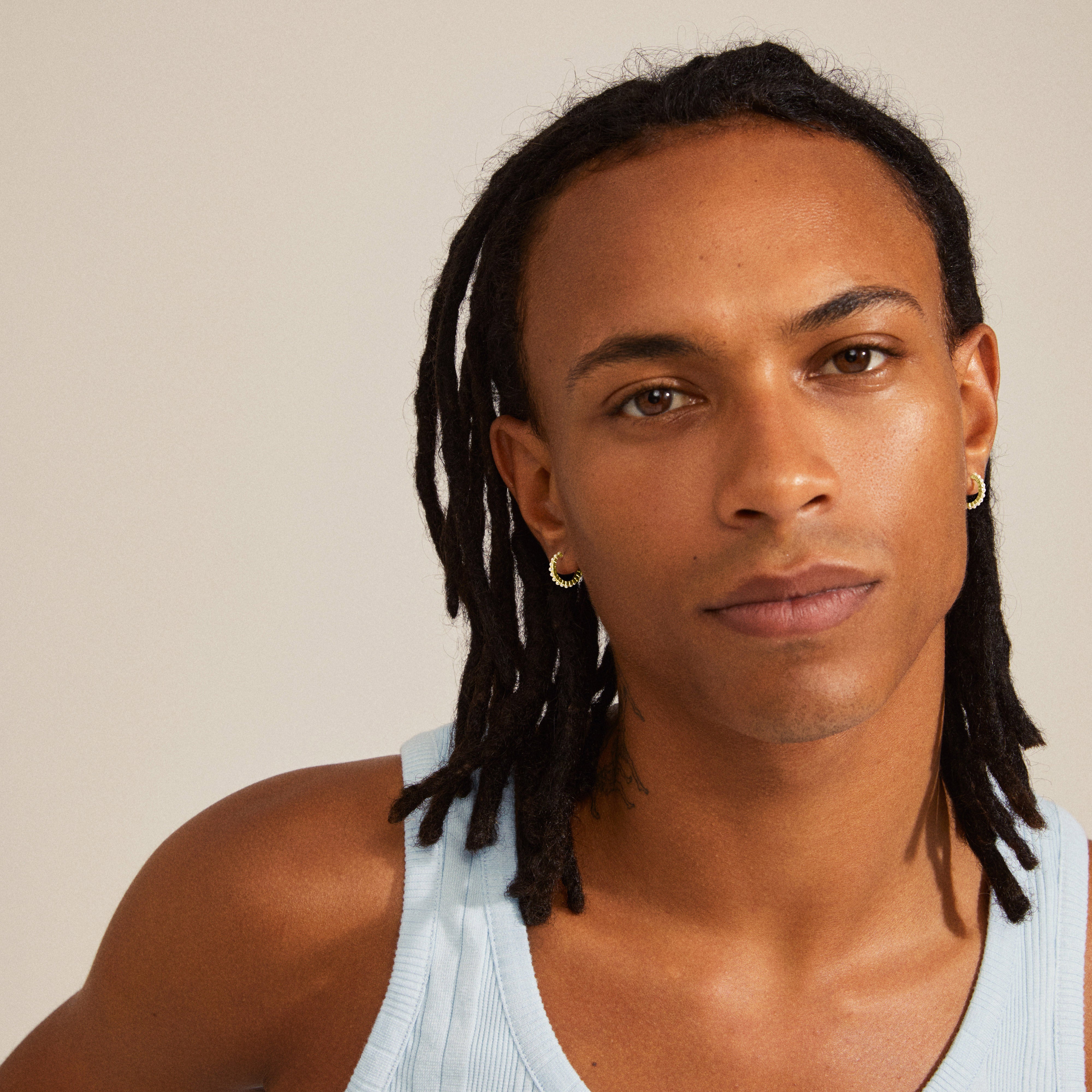 EKTA pearl huggie hoop earrings, gold-plated, showcased by a man with dreadlocks, exuding a stylish and classy vibe from Pilgrim's Classics collection.