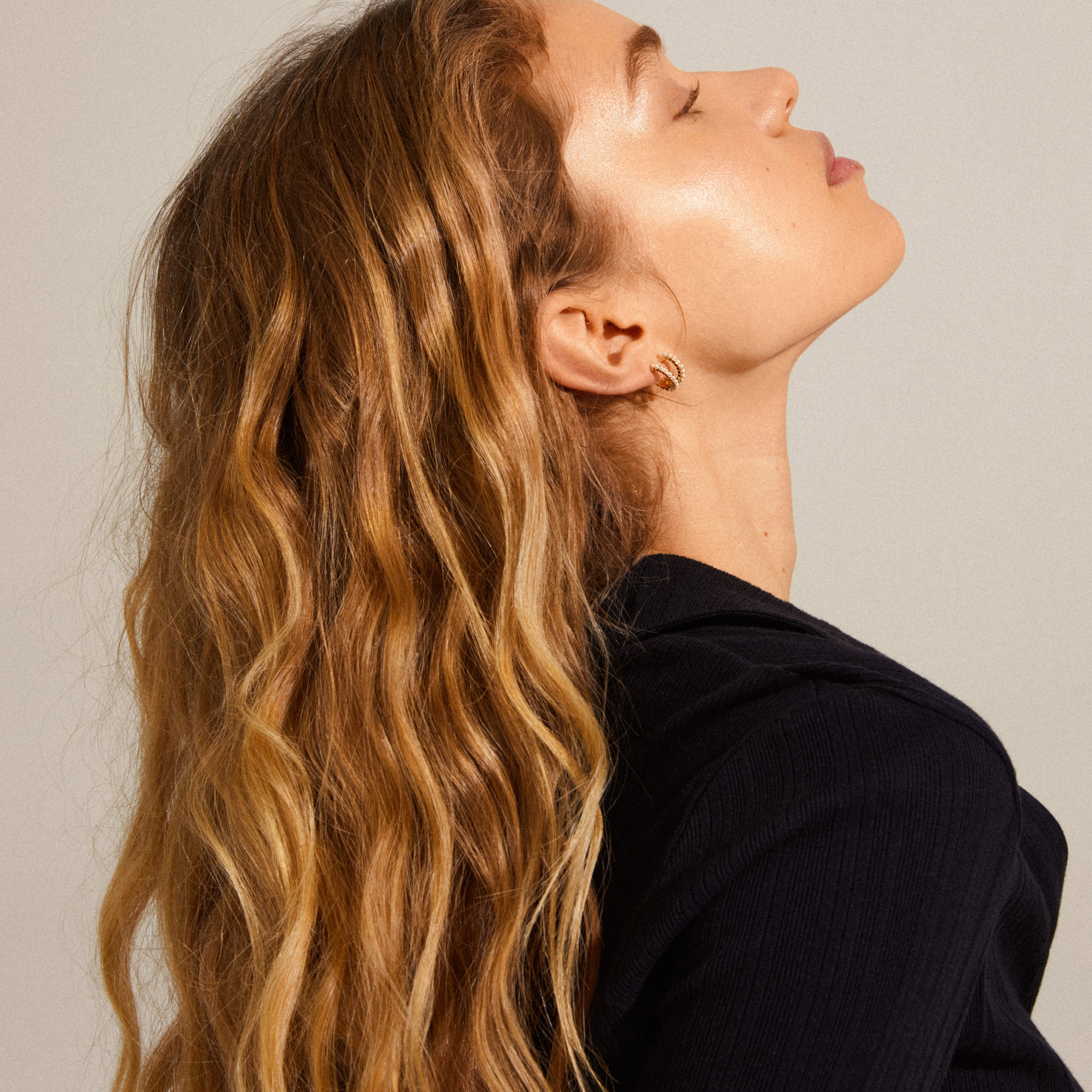 Woman wearing Ekta pearl huggie hoop earrings, gold-plated, with eyes closed, highlighting the earrings' elegant design and pearl detail from Pilgrim's Classics collection.