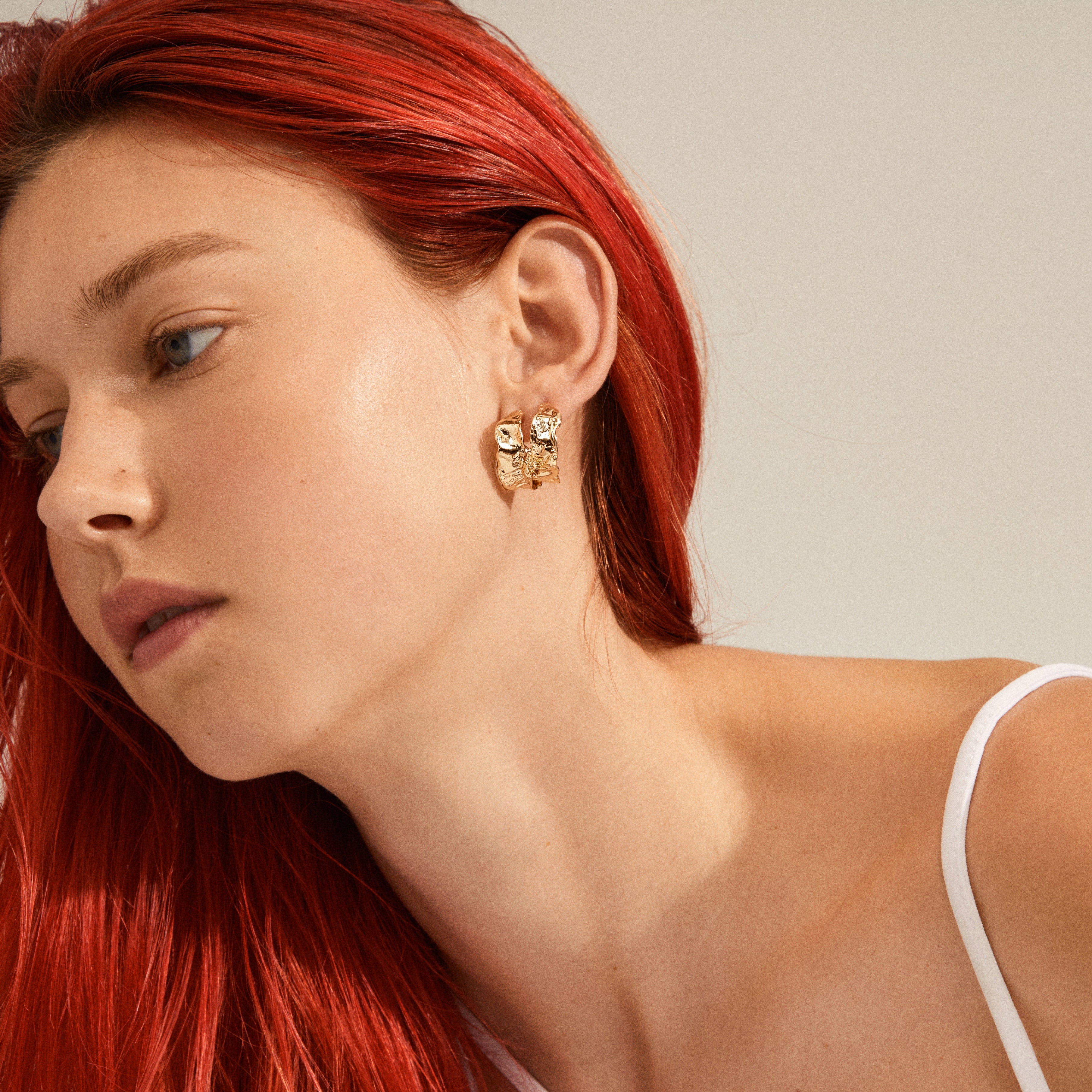 Close-up of a woman with red hair wearing ELARA organic shaped gold-plated hoop earrings, showcasing their elegant, nature-inspired design by Pilgrim.