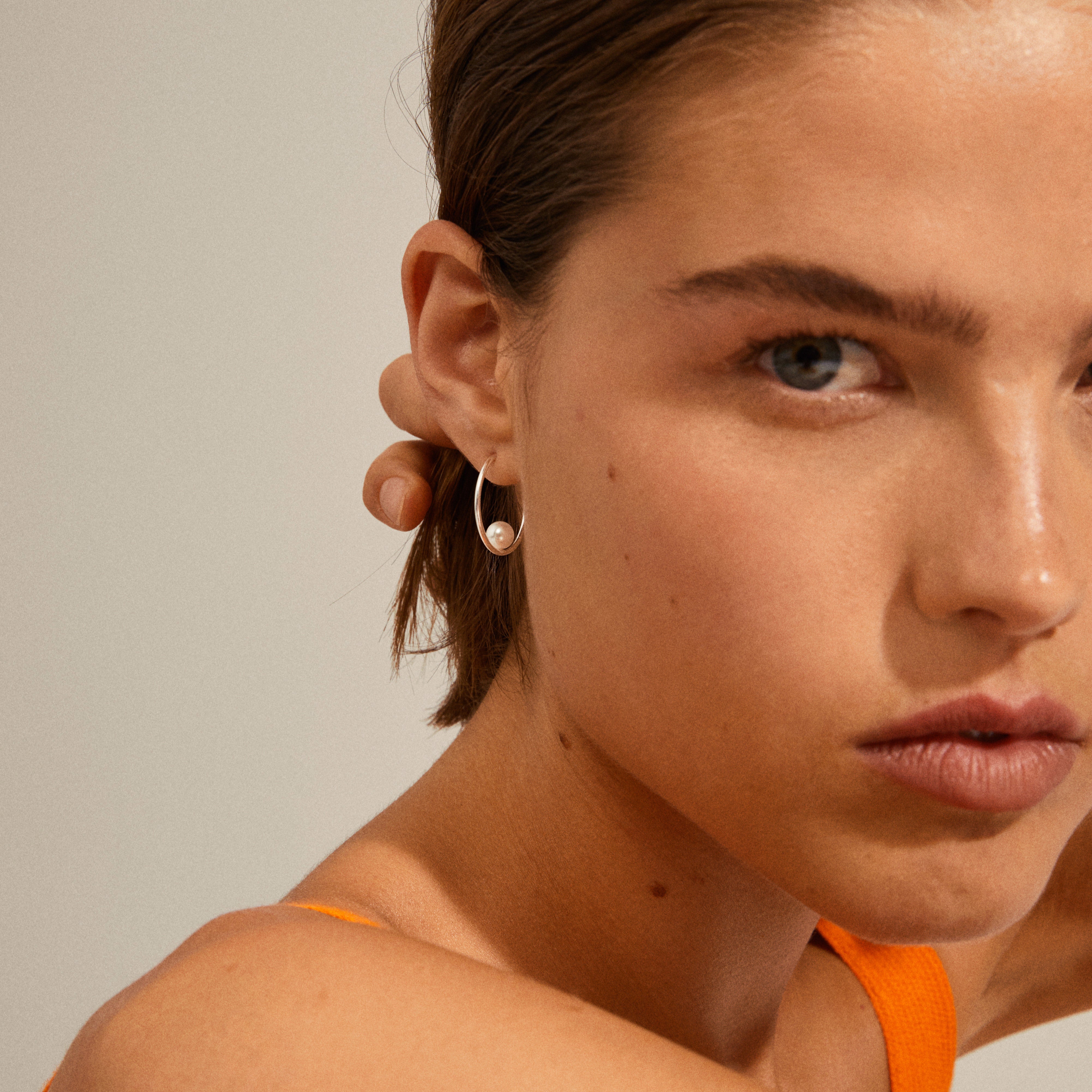 ELINE pearl hoop earrings silver-plated, featuring a slender design with a central white pearl, captured in a close-up of a woman's ear.