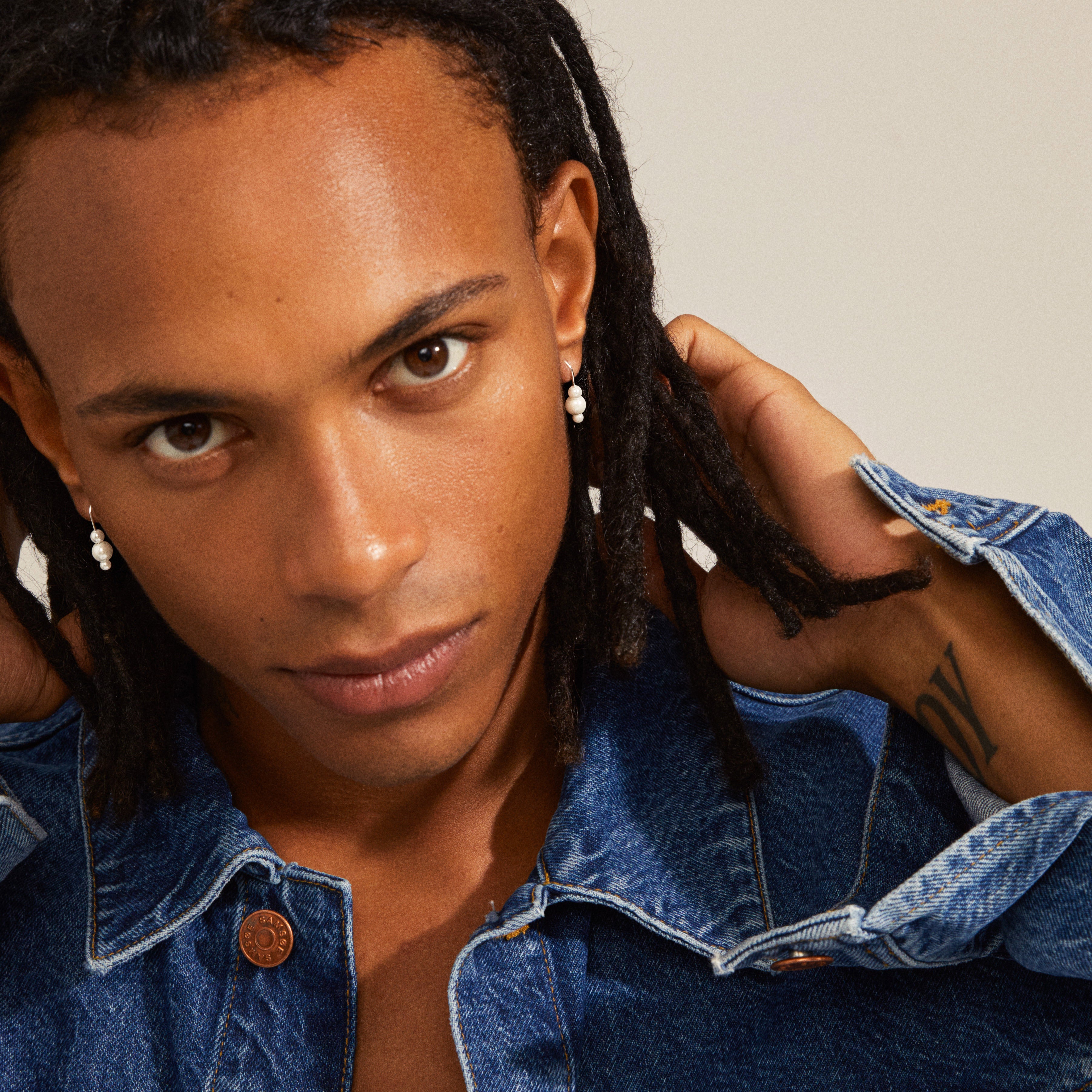 Man with dreadlocks wearing ELBERTA pearl silver-plated earrings, showcasing their elegant design and feminine, harmonious touch from Pilgrim's Classics collection.