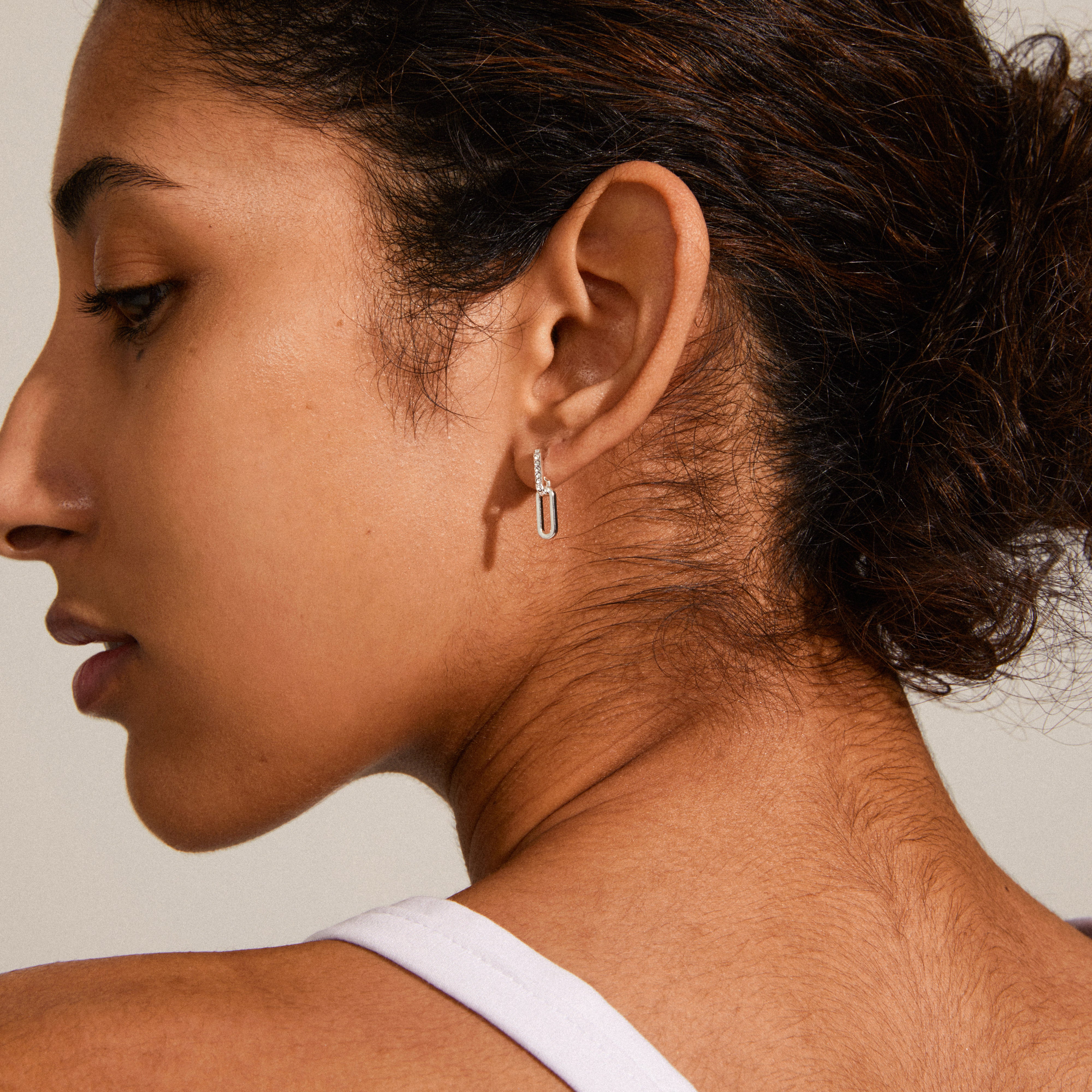 ELISE silver-plated earrings with oval links and Preciosa crystals, showcasing a minimalist, industrial style, worn by a woman with her hair pulled back.