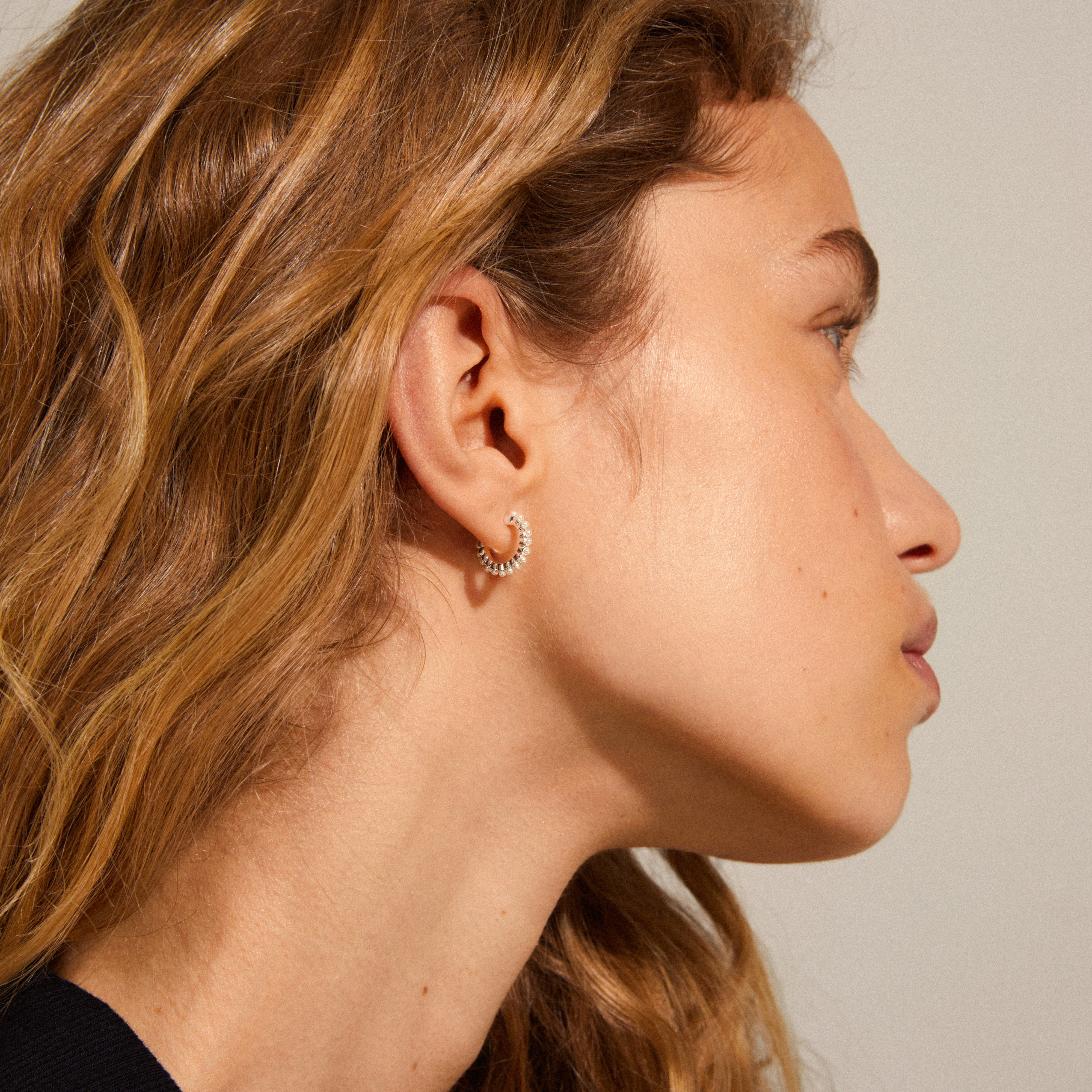 EKTA pearl huggie hoop earrings, silver-plated, elegantly showcased on a woman's ear, highlighting their feminine and classic design with beautiful pearl accents.