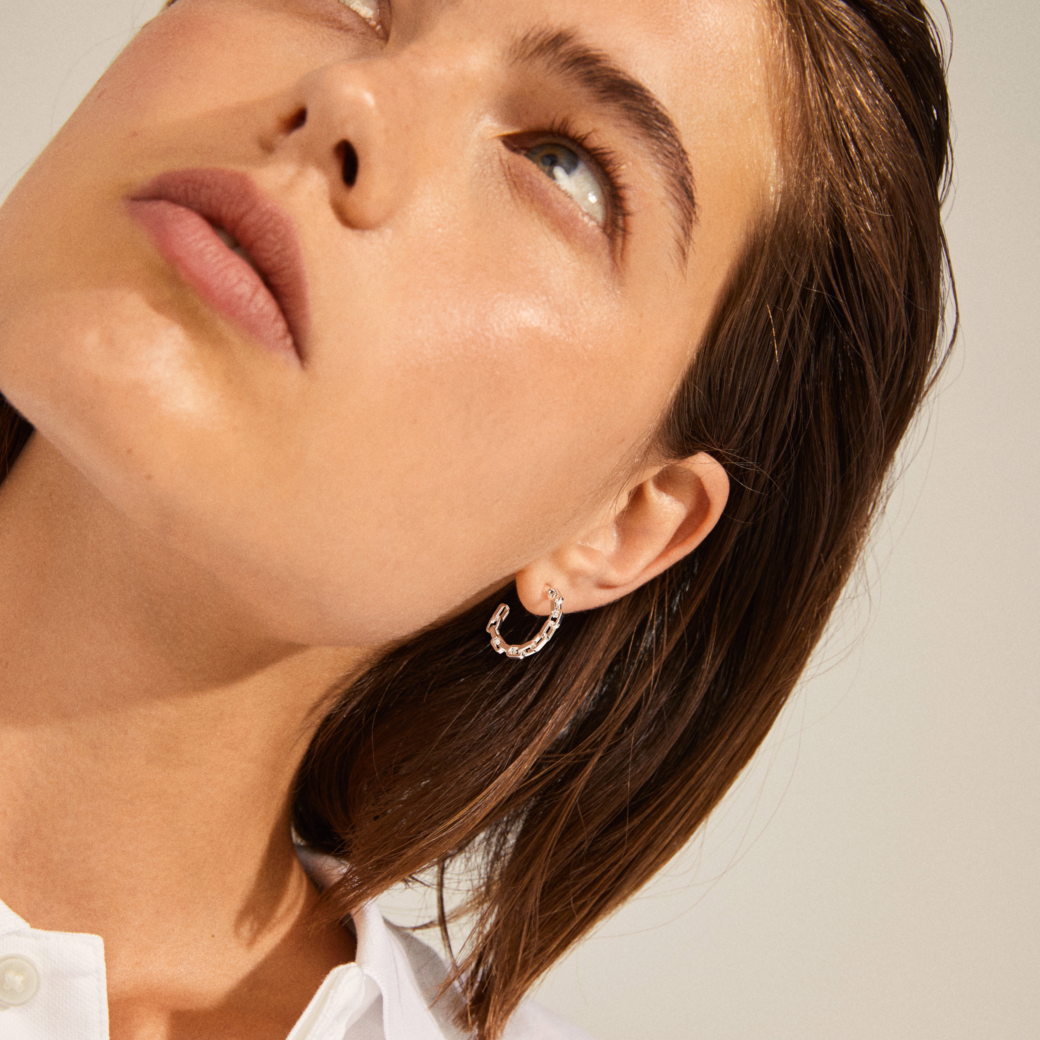Close-up of a woman wearing EIRA silver-plated cable chain hoop earrings, showcasing their minimalist and urban design with small rectangular joints.