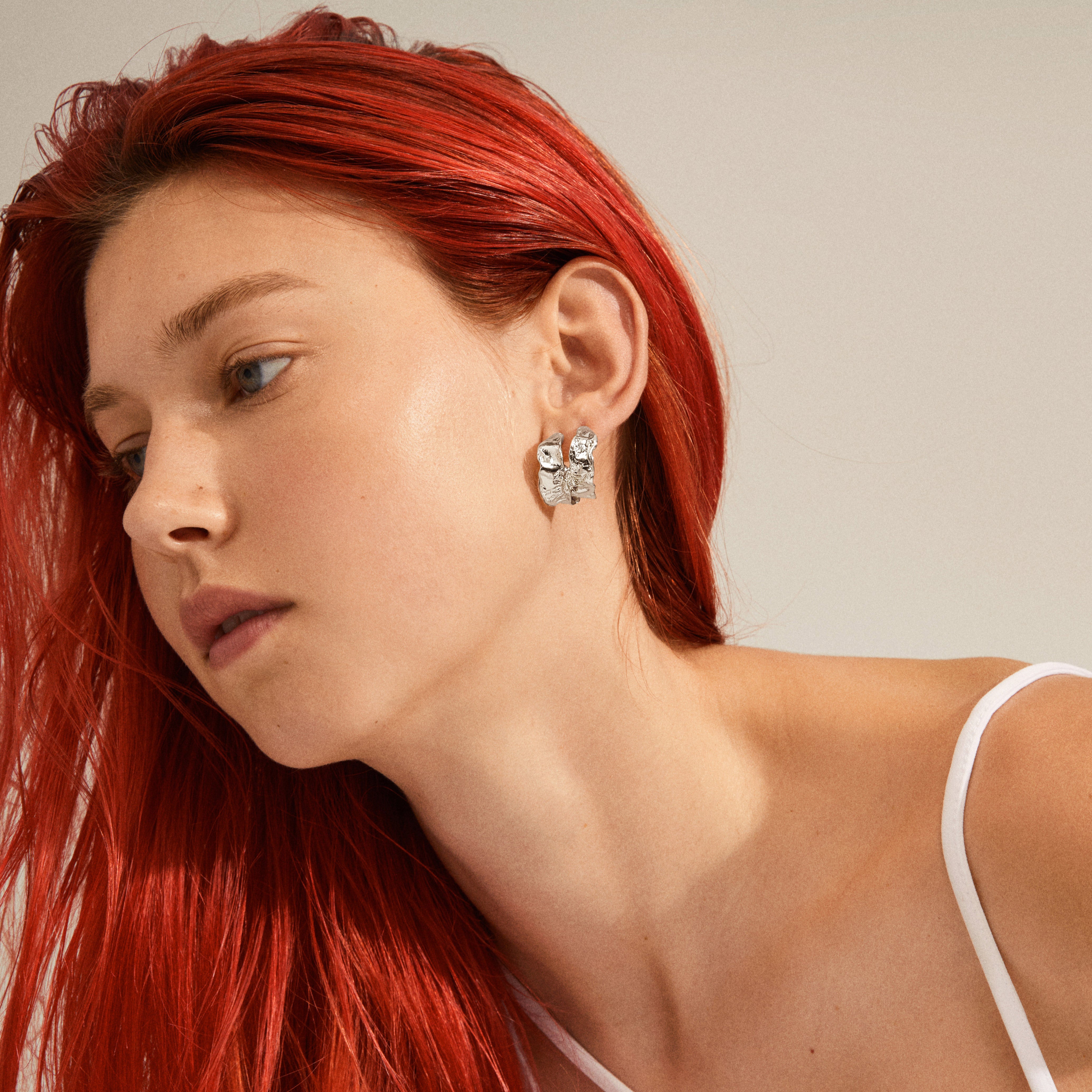 Woman with red hair wears ELARA organic-shaped hoop earrings, silver-plated, showcasing a natural, handcrafted design, highlighting Pilgrim's blend of trendy and timeless style.