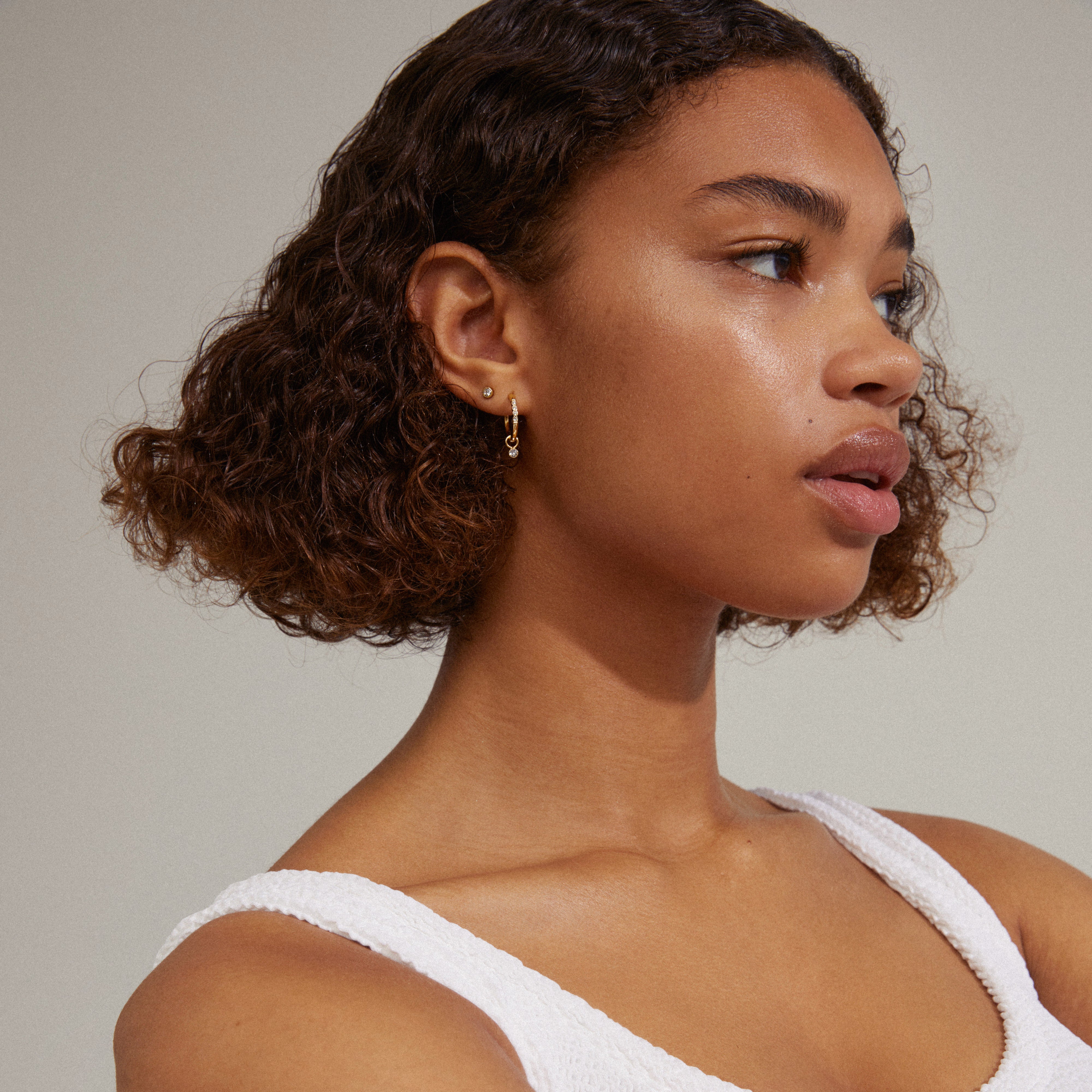 ELNA crystal earrings 2-in-1 set gold-plated, featuring classic ear studs and crystal-adorned hoops, worn by a woman with curly hair.