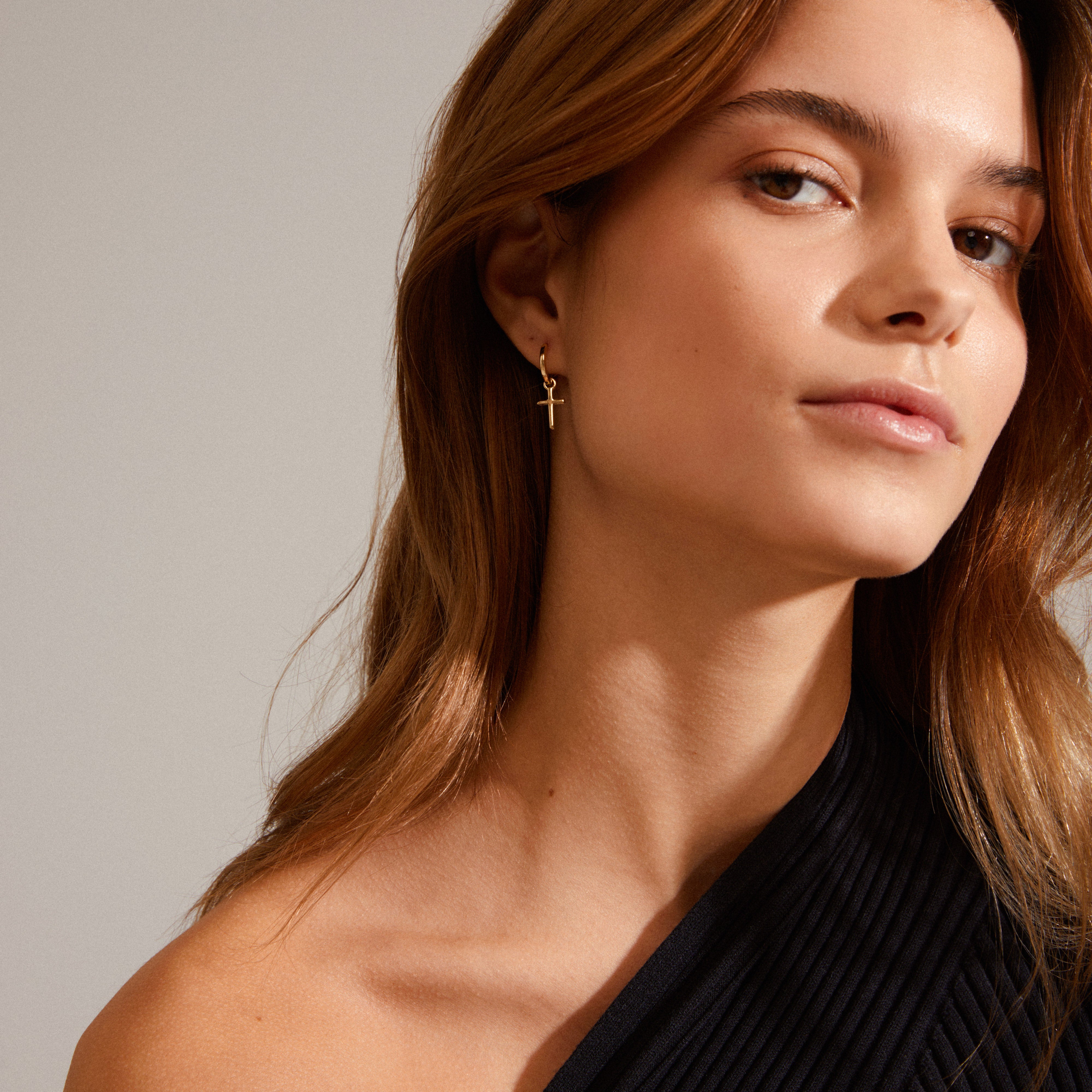 Woman wearing Pilgrim's DAISY cross hoops gold-plated, featuring simple huggie hoops with removable cross pendant, highlighting Scandinavian craftsmanship and modern style.