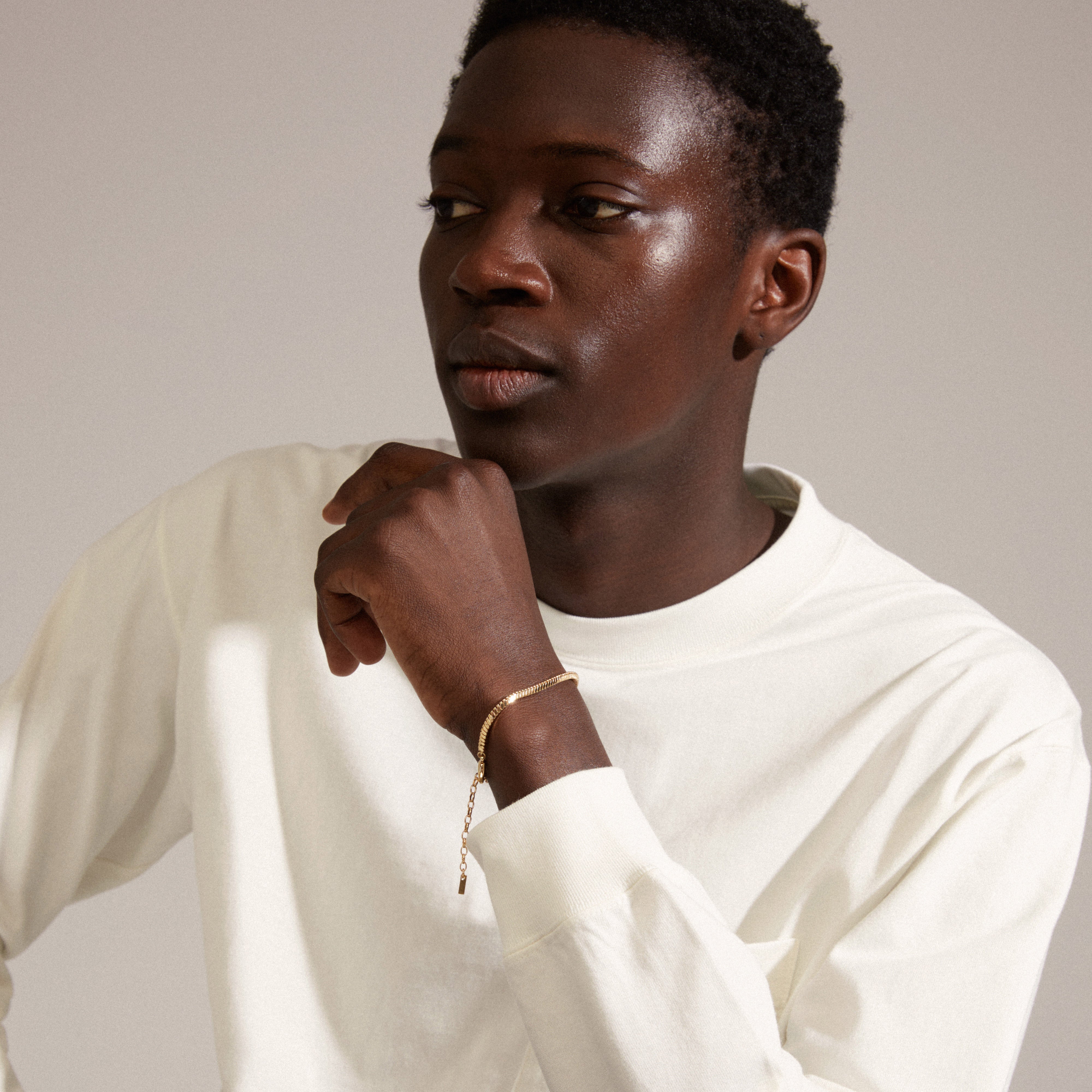 Young Black man in a white shirt showcases the DOMINIQUE gold-plated bracelet by Pilgrim, featuring a square snake chain with a delicate hanging chain detail.