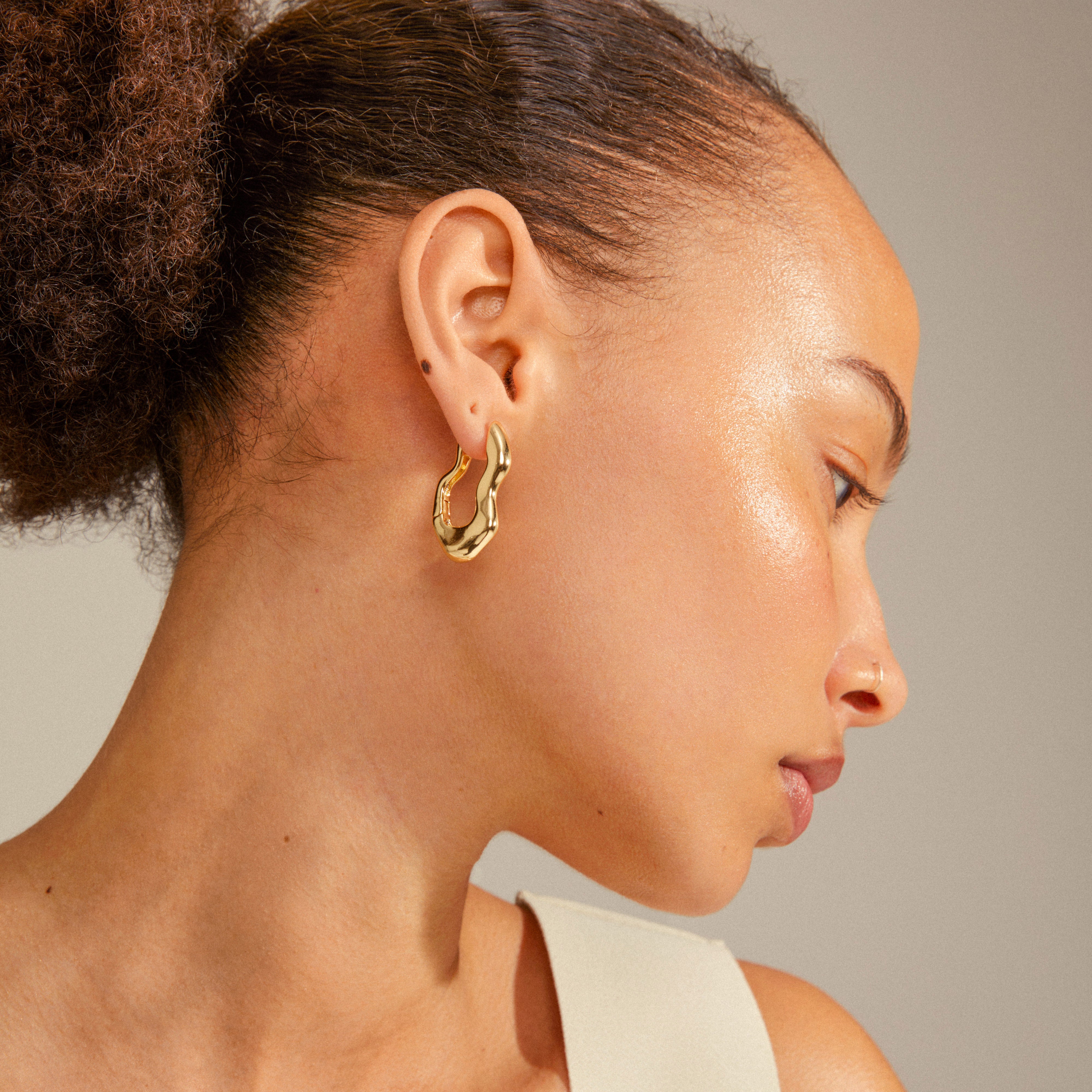 Close-up of a woman's ear wearing LOULIA wavy gold-plated earrings with an organic silhouette and easy click clasp.