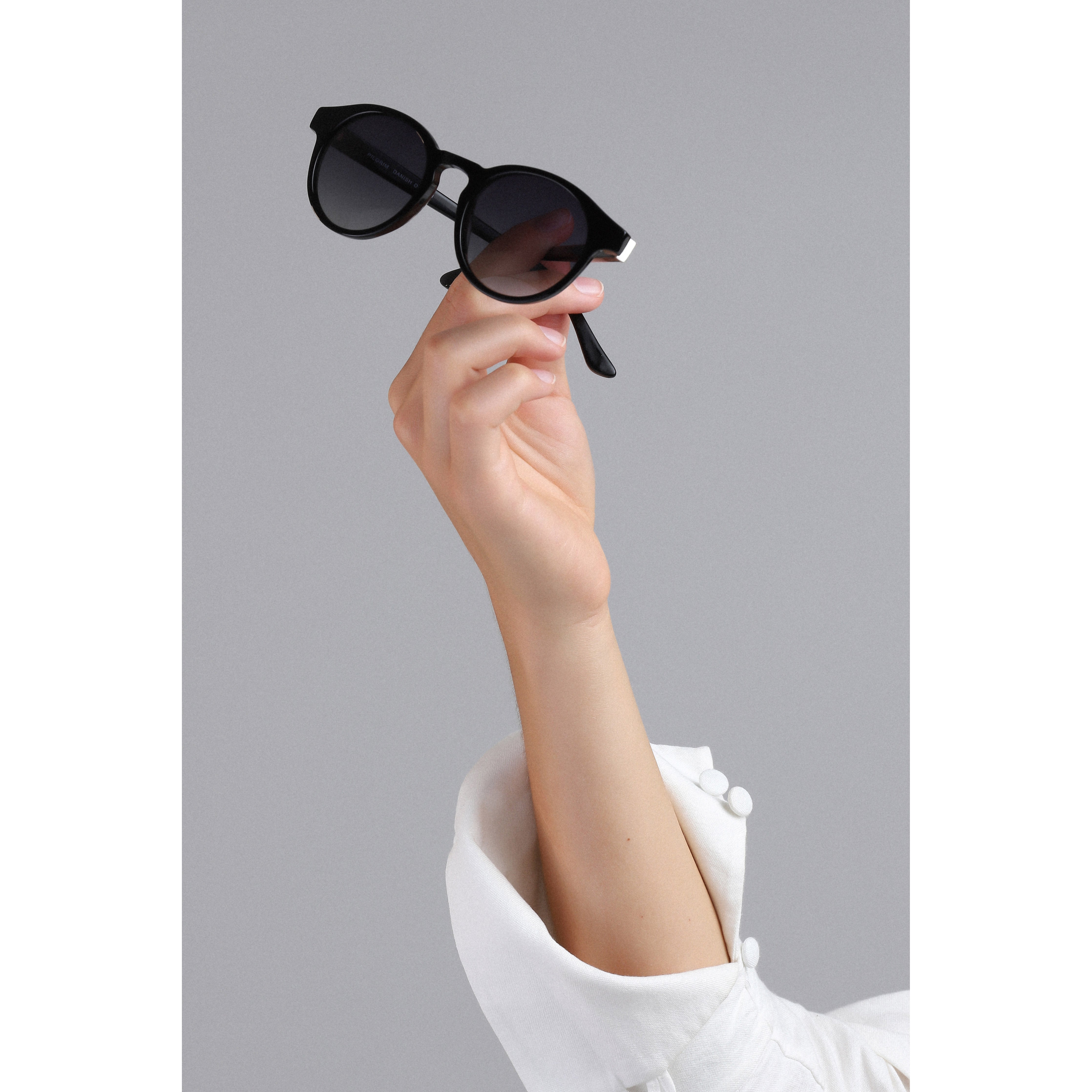 Hand holding Meriel Black sunglasses, showcasing elegant round frames with discreet metal detail near the temples, offering stylish sun protection.