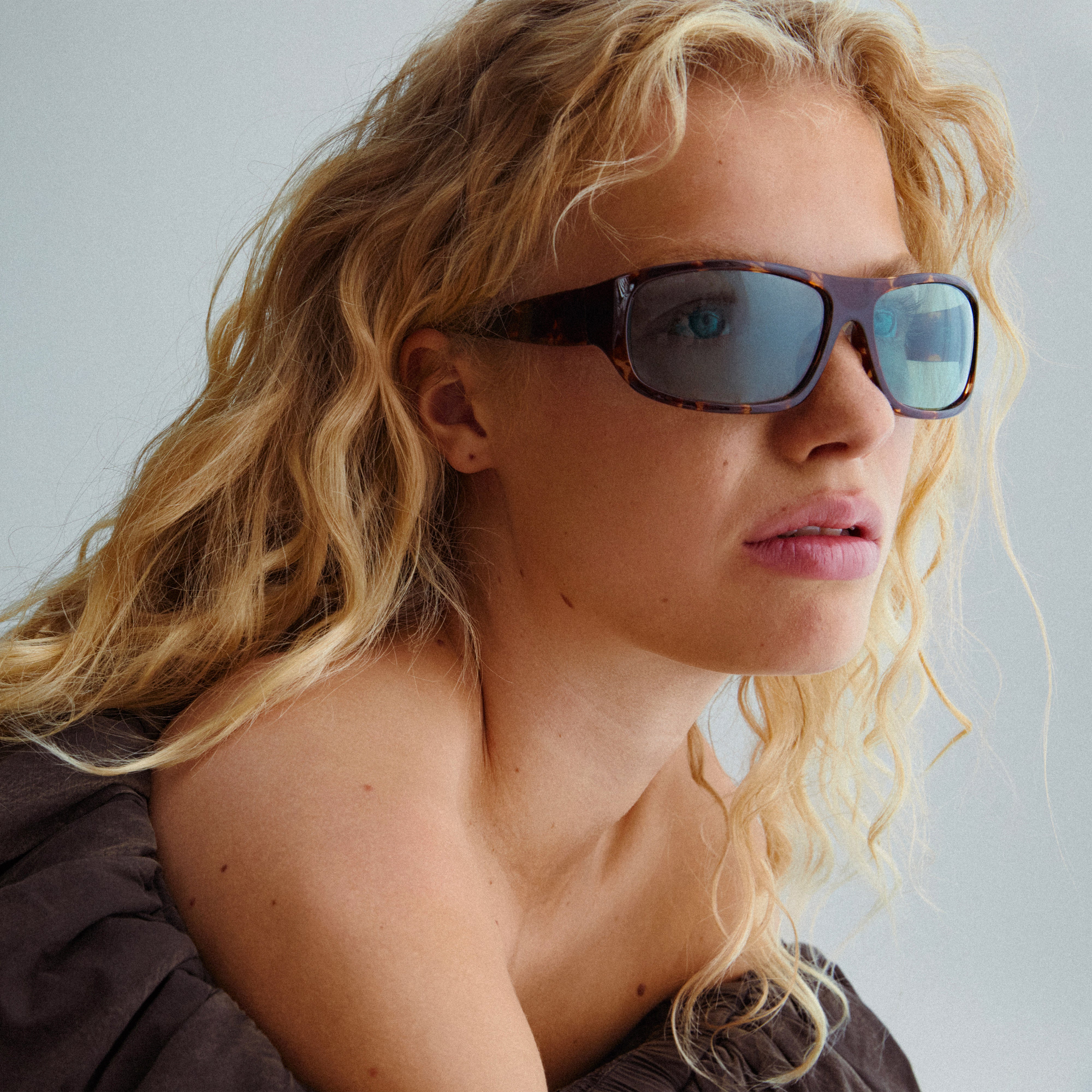 Woman with blonde hair wearing GERTRUD sunglasses in tortoise brown, showcasing Pilgrim's classic design with trendy light blue lenses.