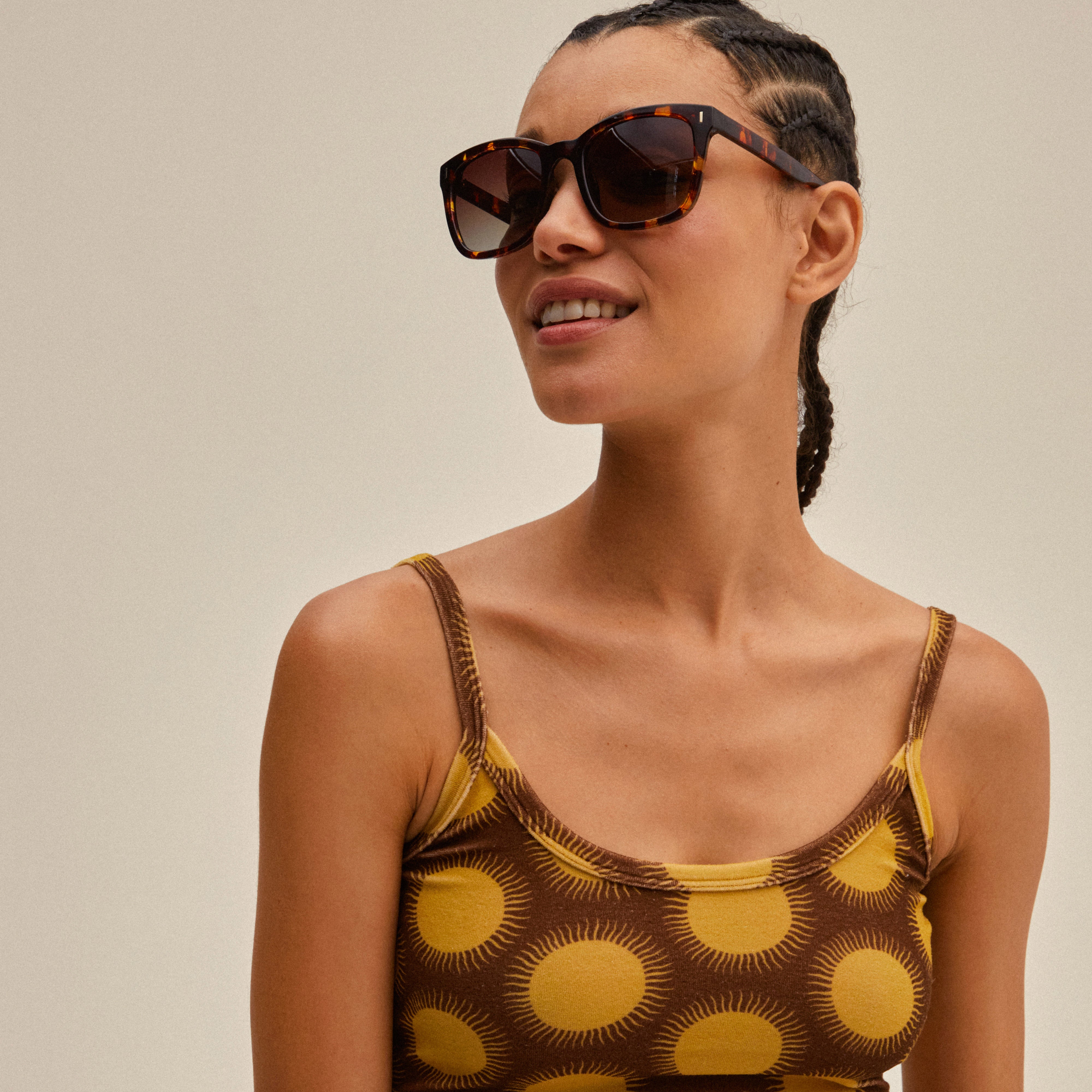 KATYA sunglasses in tortoise-brown frames, worn by a smiling woman, embody a classic, trendy style with UVA/UVB protection and sustainable features.