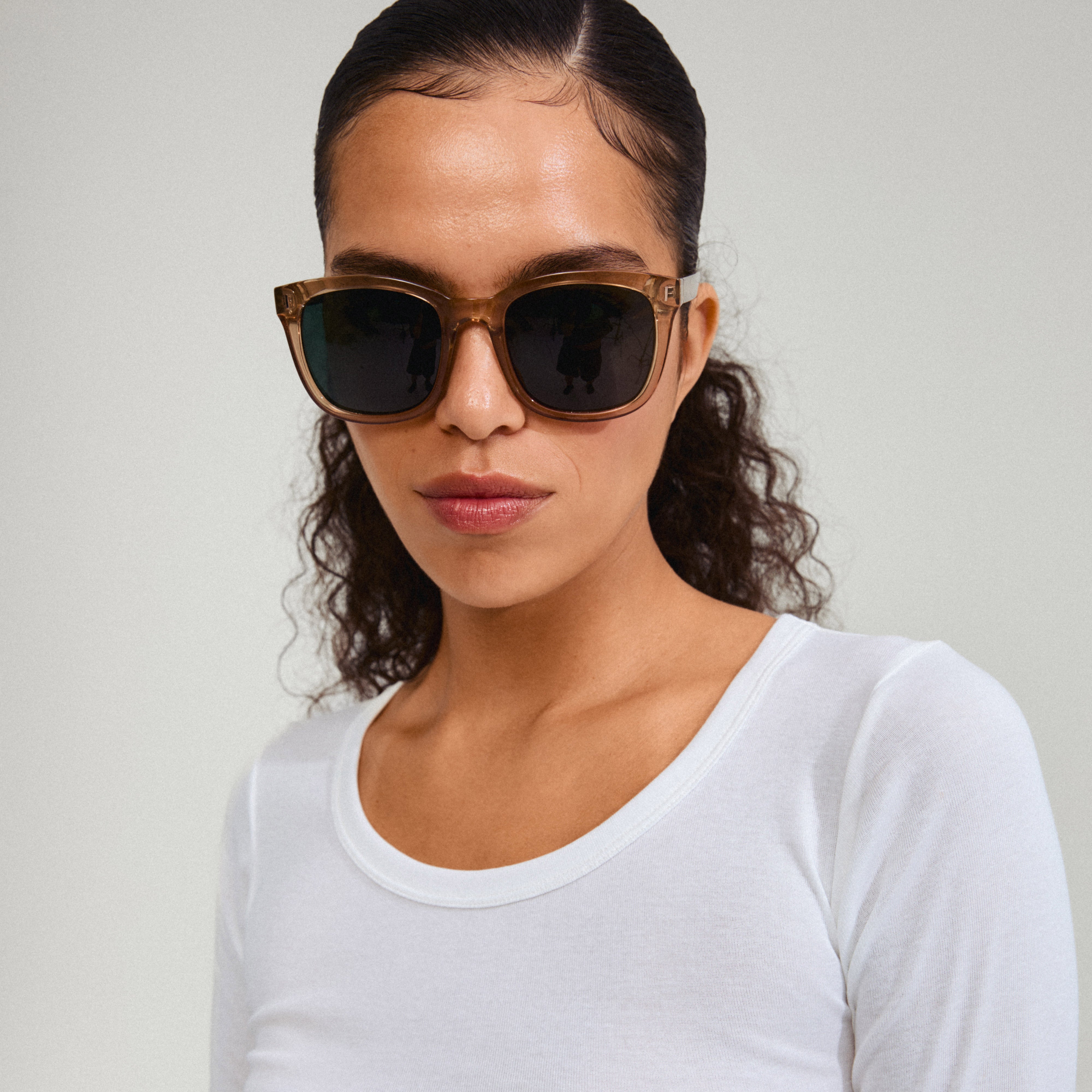 Woman wearing KATYA sunglasses in light brown, featuring transparent frames and dark green lenses, embodying Pilgrim's blend of timeless style and Scandinavian quality.