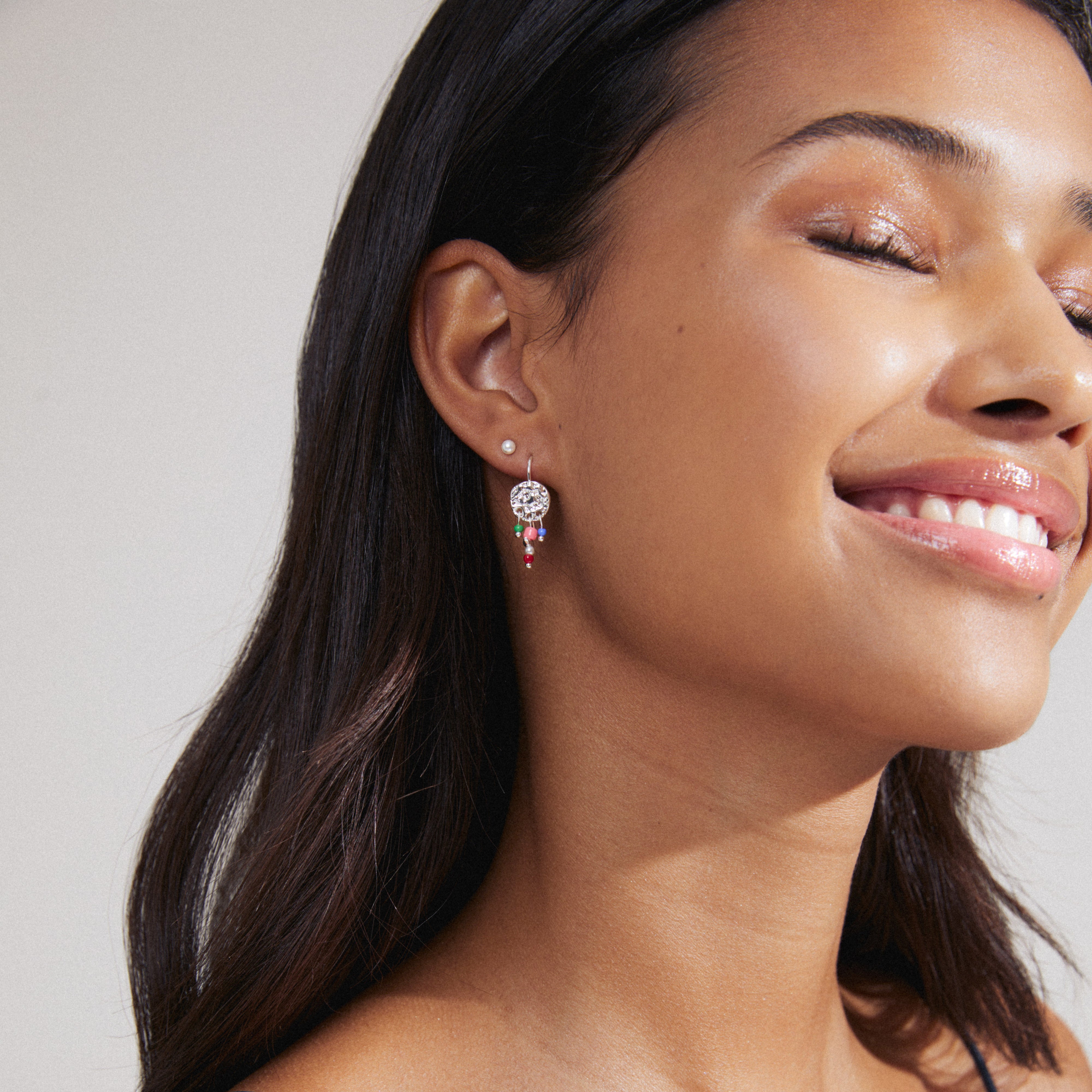 MSF earrings 2-in-1 set silver-plated, features playful, colourful beaded pendants and coin earrings, supporting Médecins Sans Frontières. Woman wearing earrings with eyes closed.