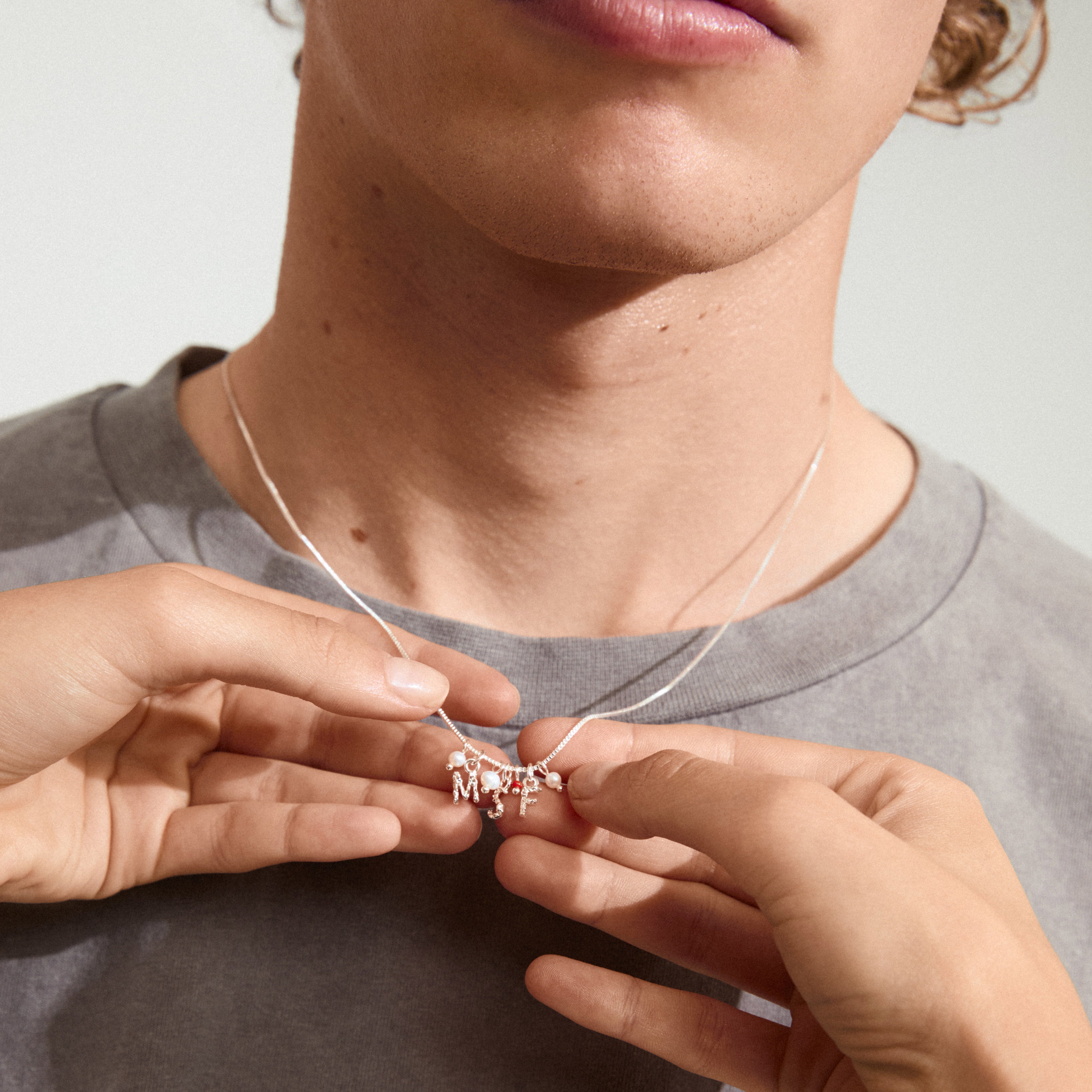 Silver-plated MSF charity necklace with petite freshwater pearls and red micro pearl, held by a person, symbolizing support for Doctors Without Borders.