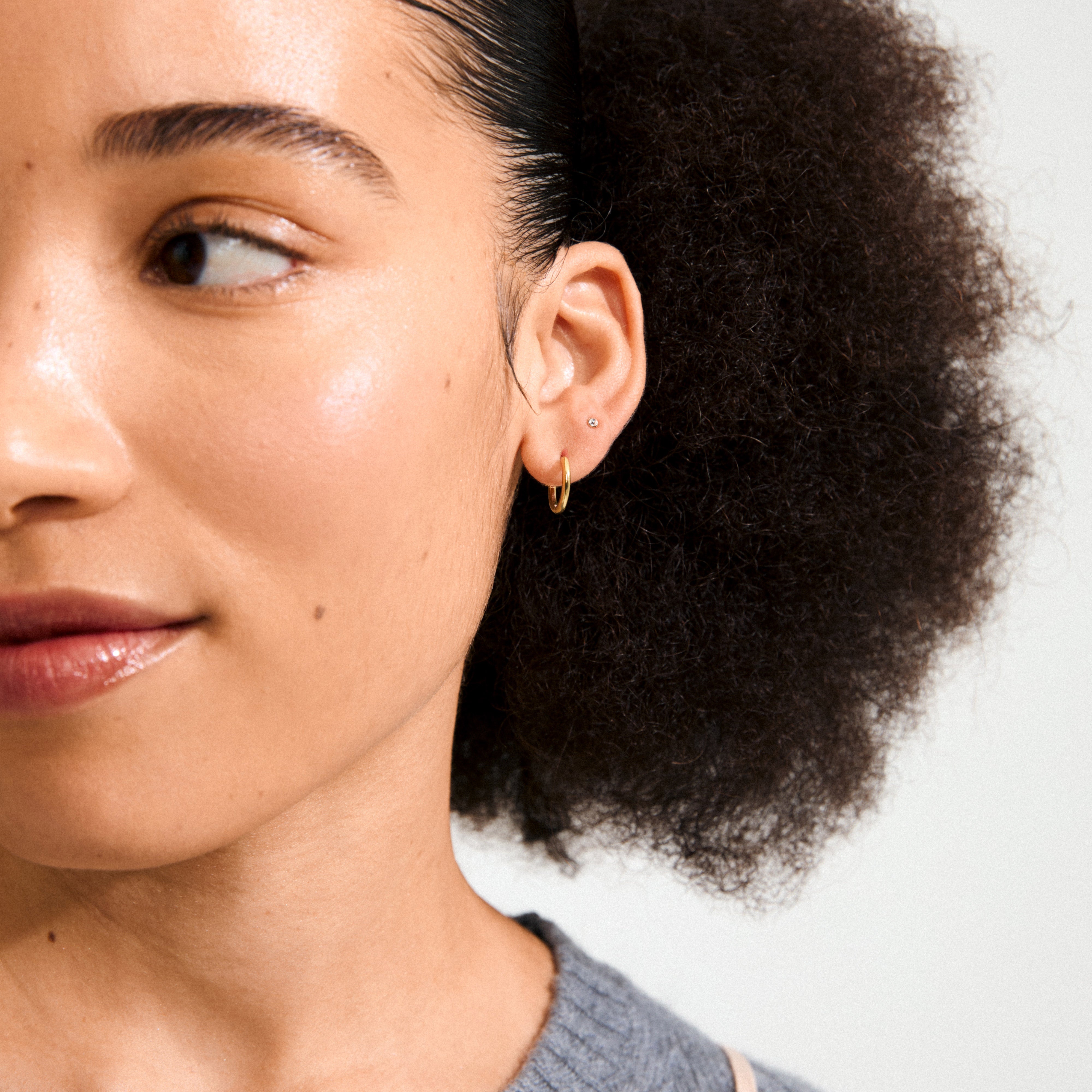 Young woman wearing HALO gift set earrings, showing a small stud and gold hoop on her earlobe, highlighting Pilgrim's blend of timeless and trendy jewellery.