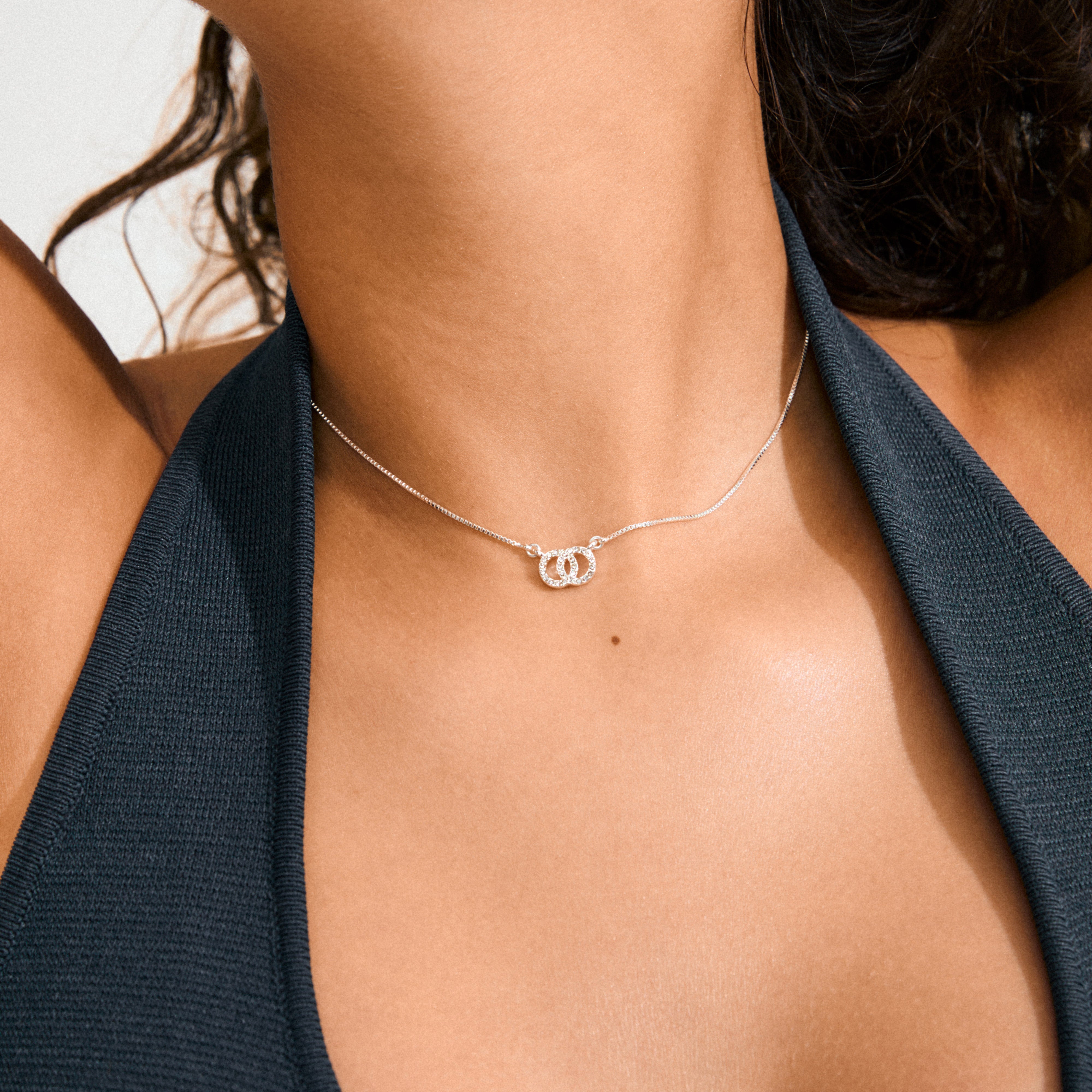 Close-up of HARLAN gift set: silver-plated necklace with interlocking ring pendant, featuring sparkling crystals, elegantly worn with a matching pair of stud earrings.