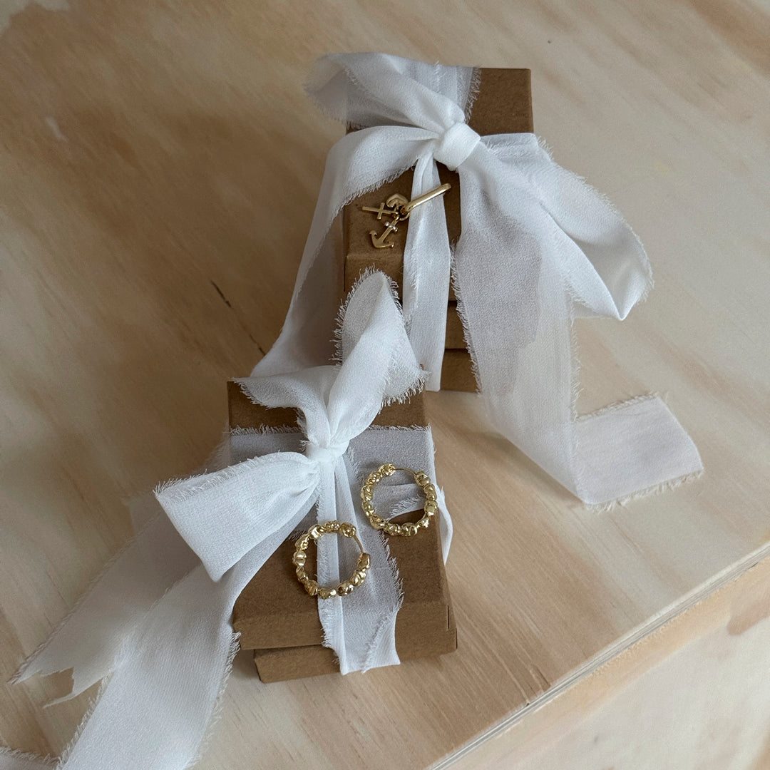 A pair of gift boxes tied with white ribbons, featuring gold hoop earrings, embodying Pilgrim's blend of timeless and trendy Danish jewelry.