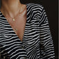Woman wearing a zebra print shirt, showcasing the VALKYRIA coin necklace 2-in-1 set, featuring gold-plated chains with rustic Norse mythology-inspired serpent and raven motifs.