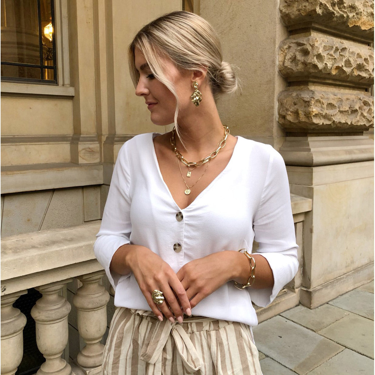 Woman wearing VALKYRIA coin necklace 2-in-1-set gold-plated, featuring Norse serpent and raven charms, standing outside a building.