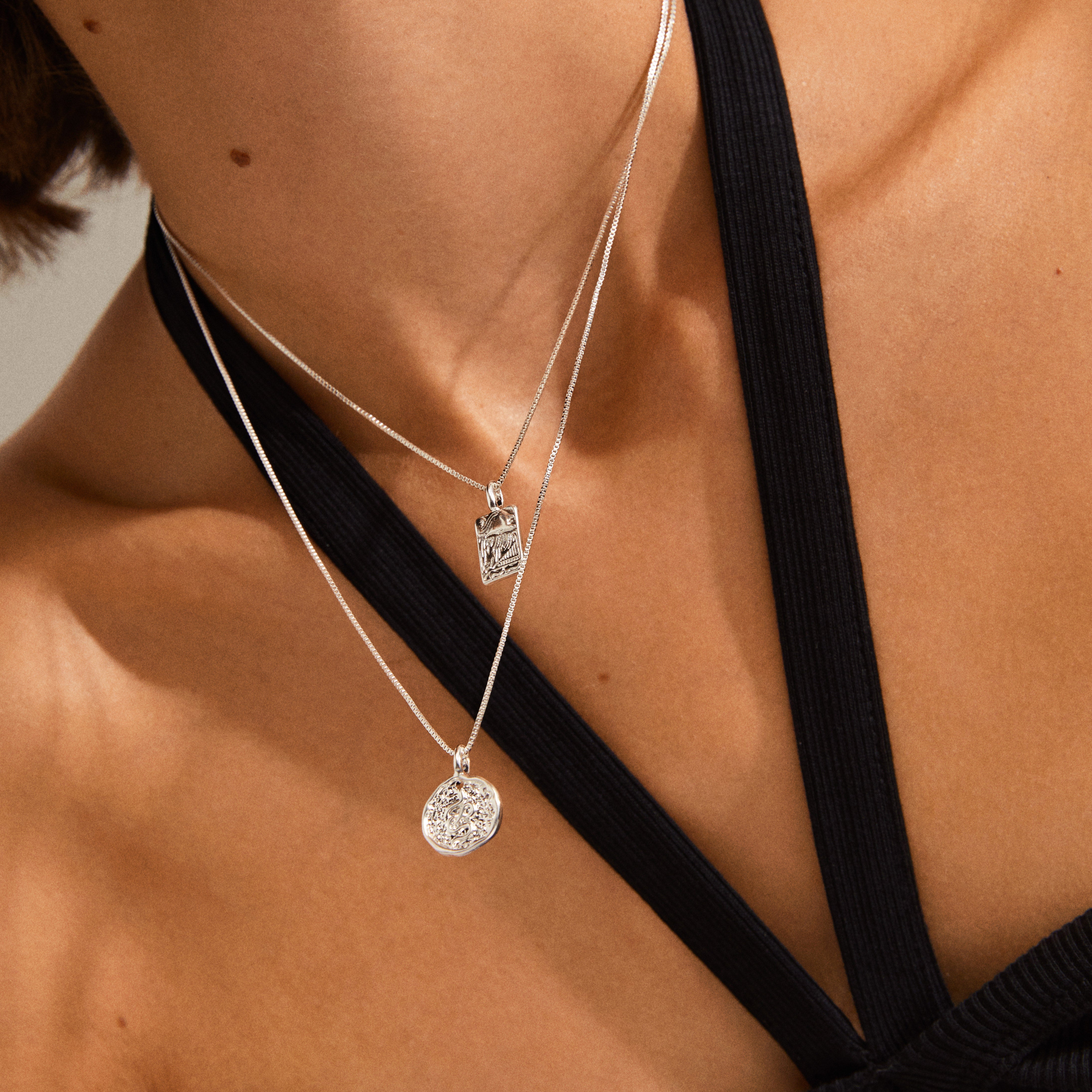 Close-up of a woman wearing the VALKYRIA coin necklace 2-in-1-set, featuring silver-plated chains with serpent and raven pendants inspired by Norse mythology.